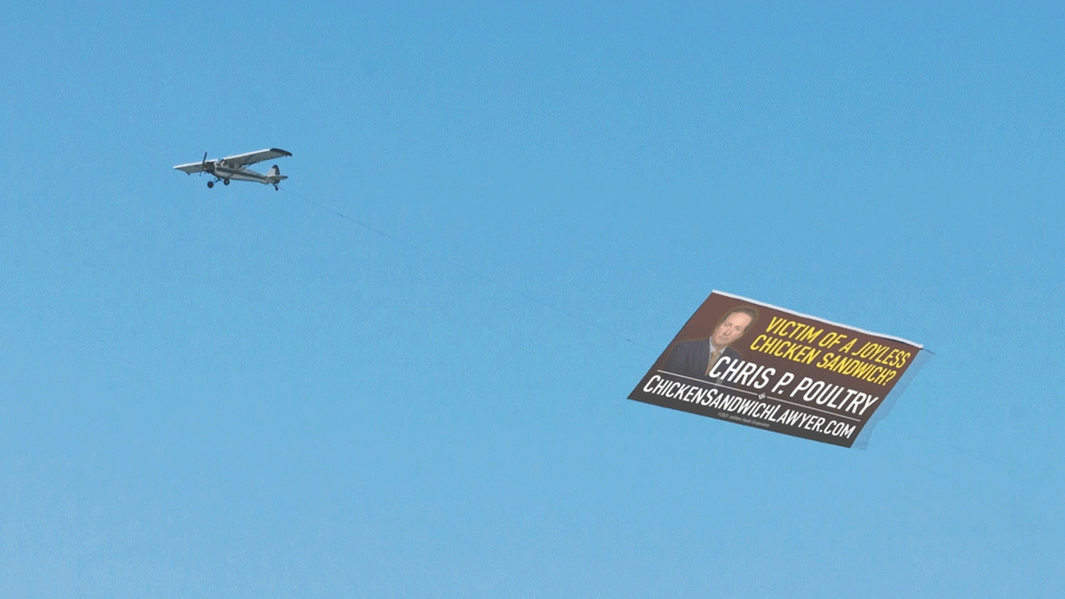 Small airplane towing a political advertisement banner in a clear blue sky.