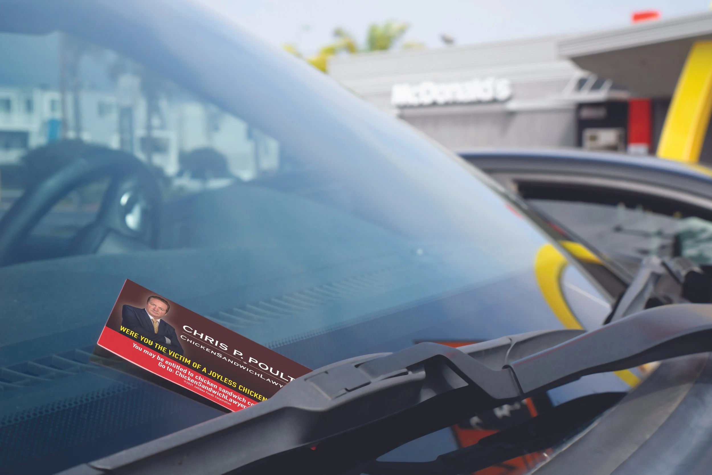 A car windshield with a political campaign flyer featuring a man in a suit and tie, with yellow and red text, partially visible on the driver's side.