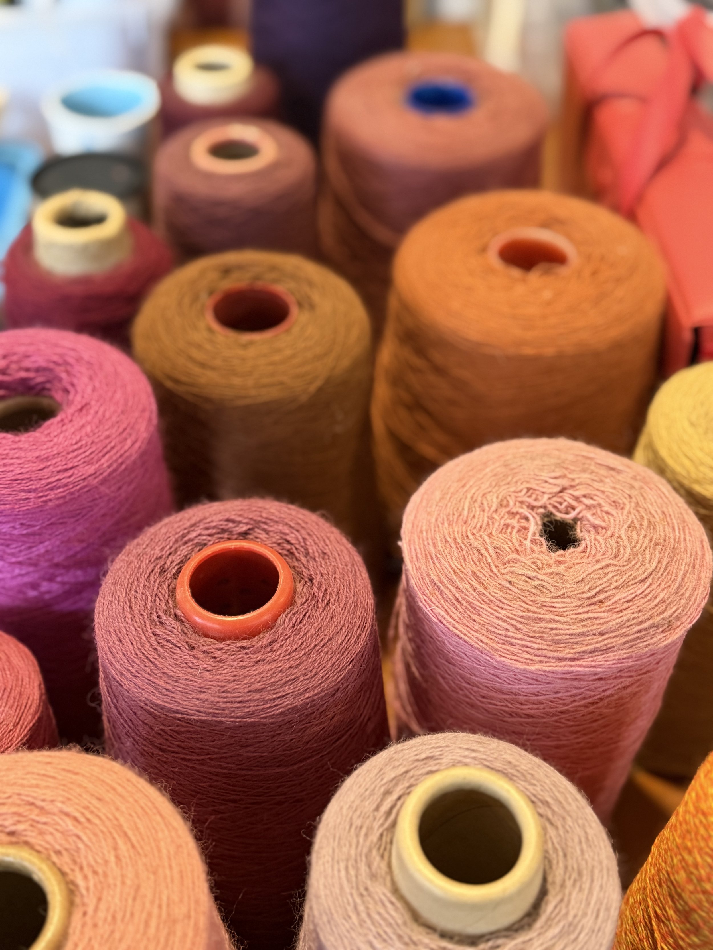 Close-up of multiple spools of yarn in shades of pink, orange, yellow, and purple.