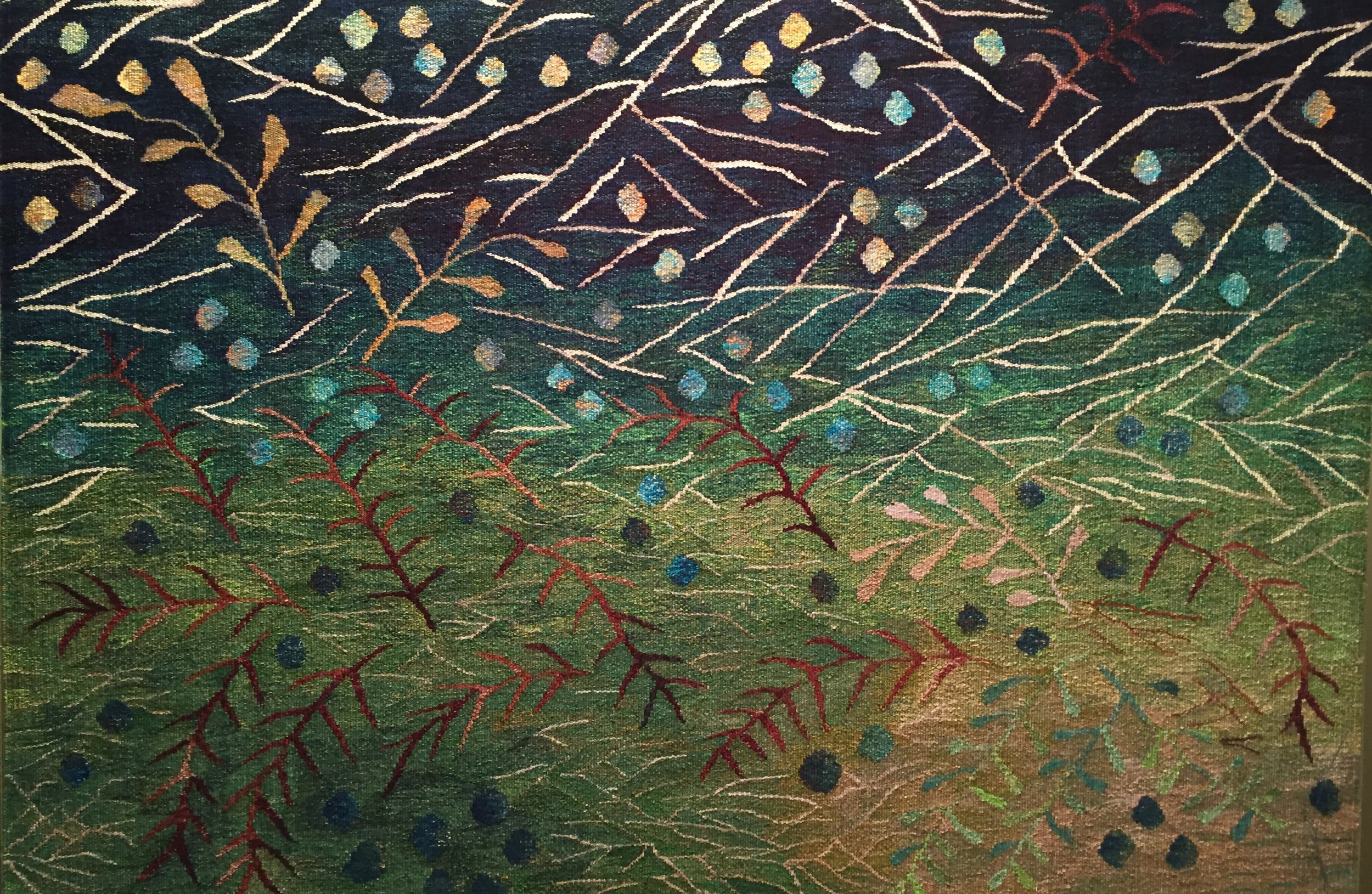 Large woven tapestry with colorful thread patterns of leaves and dots on a dark background.