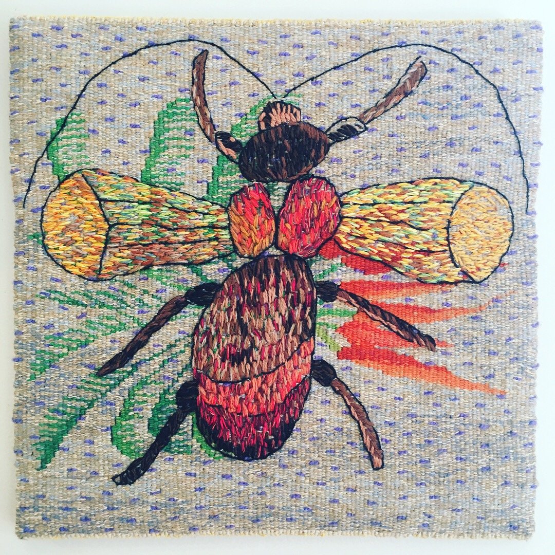 Woven Tapestry artwork of an insect with colourful wings on a fabric background with green leaves and purple accents.