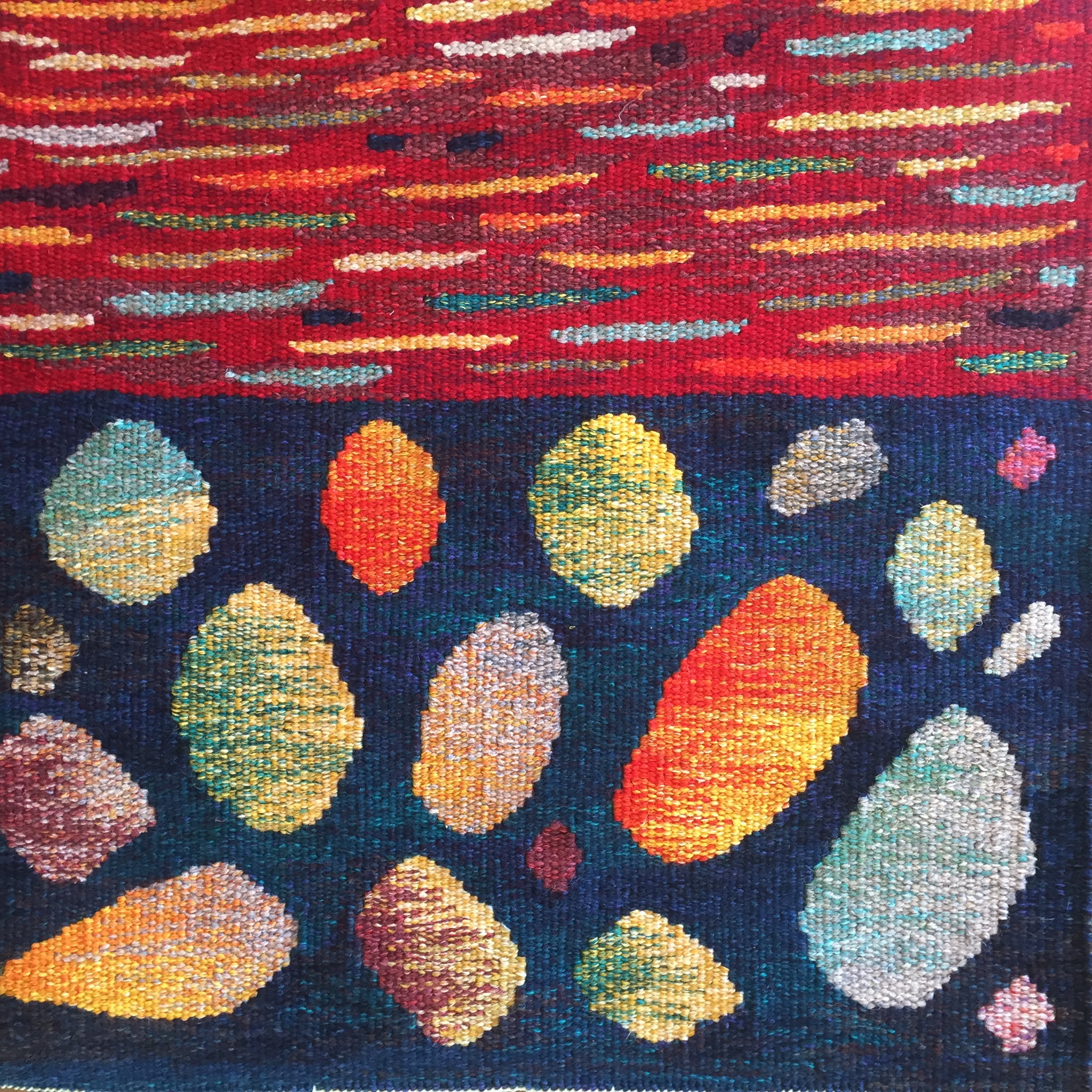 Close-up of a colorful, textured woven tapestry with abstract patterns in red, yellow, orange, white, blue, and green