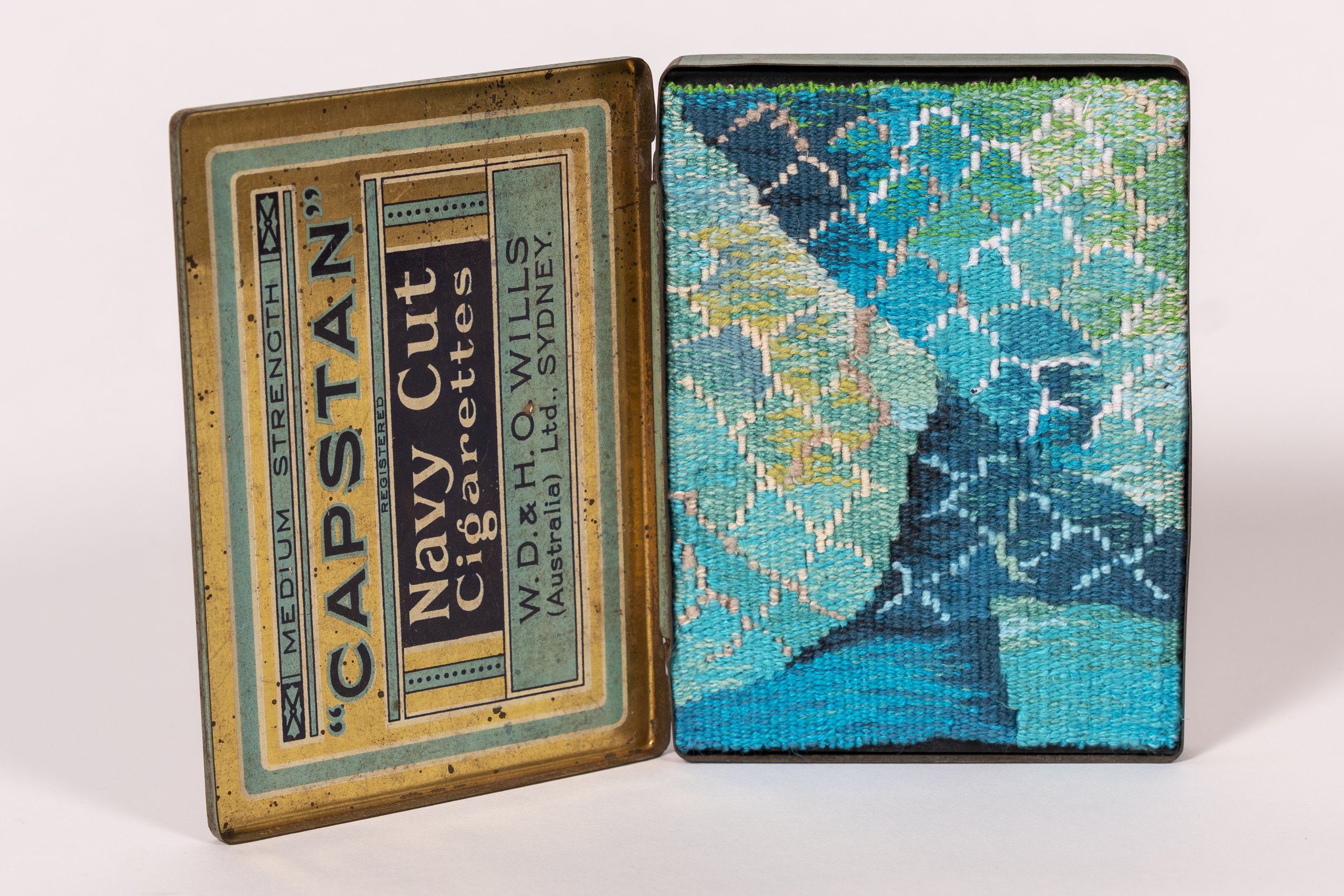 An open vintage metal box with a colorful woven tapestry inside.