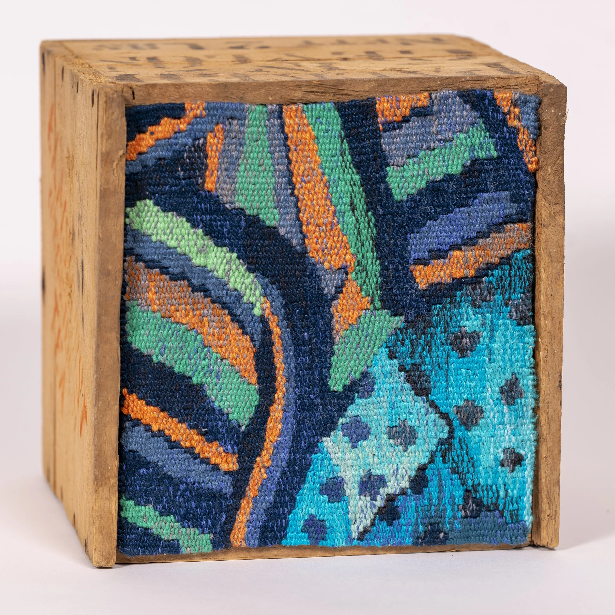 Close-up of a wooden block with multicolored woven fabric attached to one side.