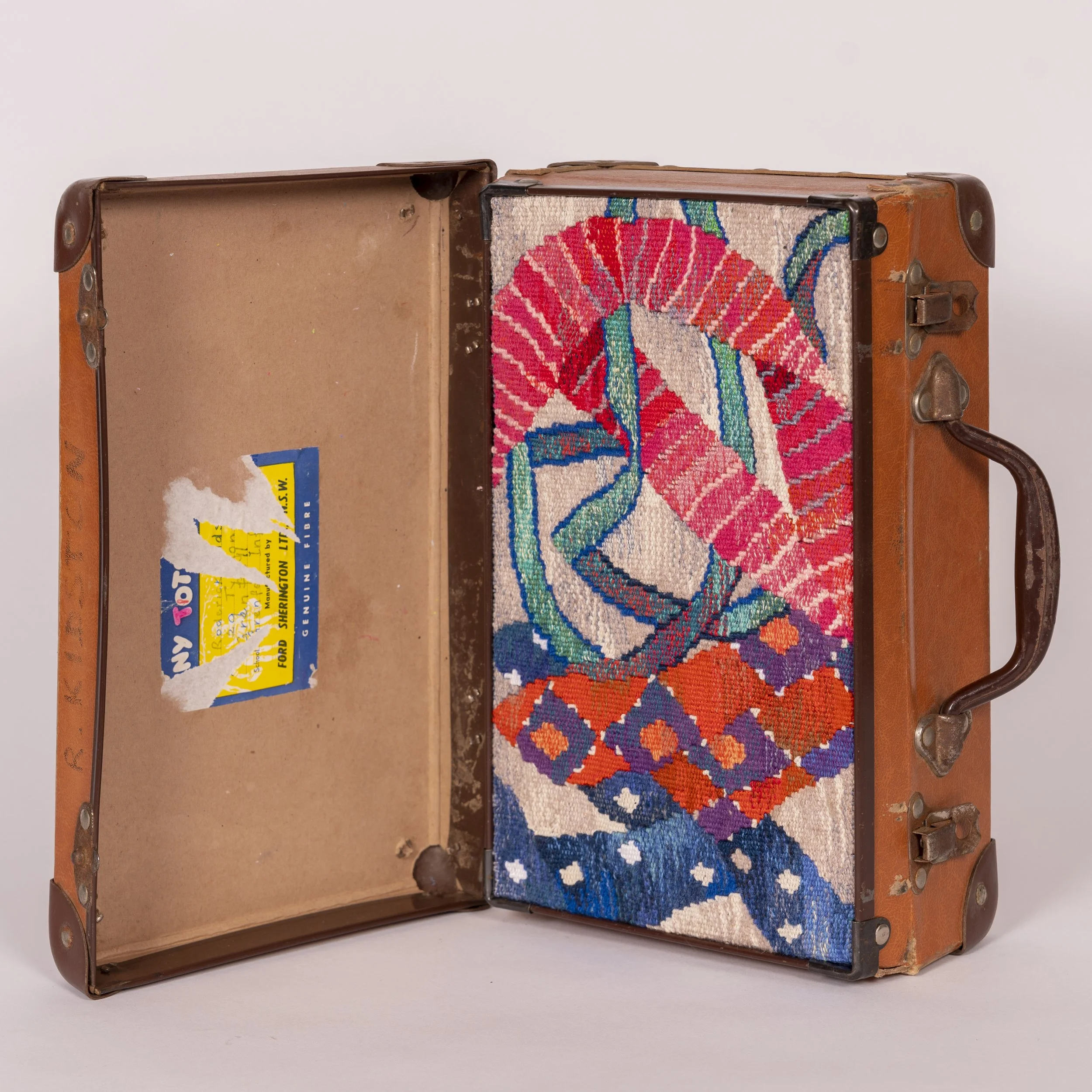 An open vintage leather suitcase with a colorful woven fabric inside, against a plain white background.