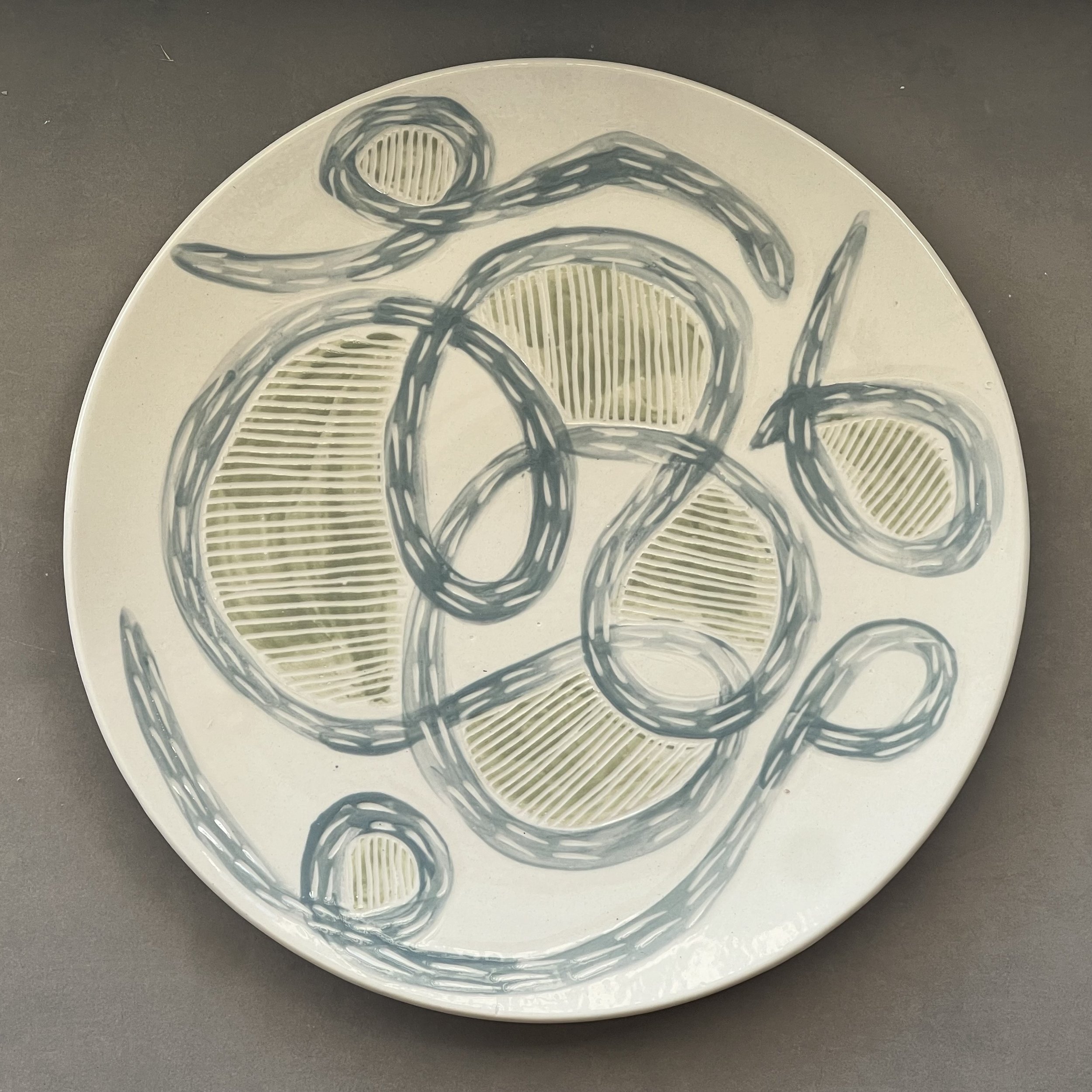 Dimity Kidston sgraffito hand carved ceramic plate with a decorative design of abstract gray lines and yellow oval shapes, set against a gray background.