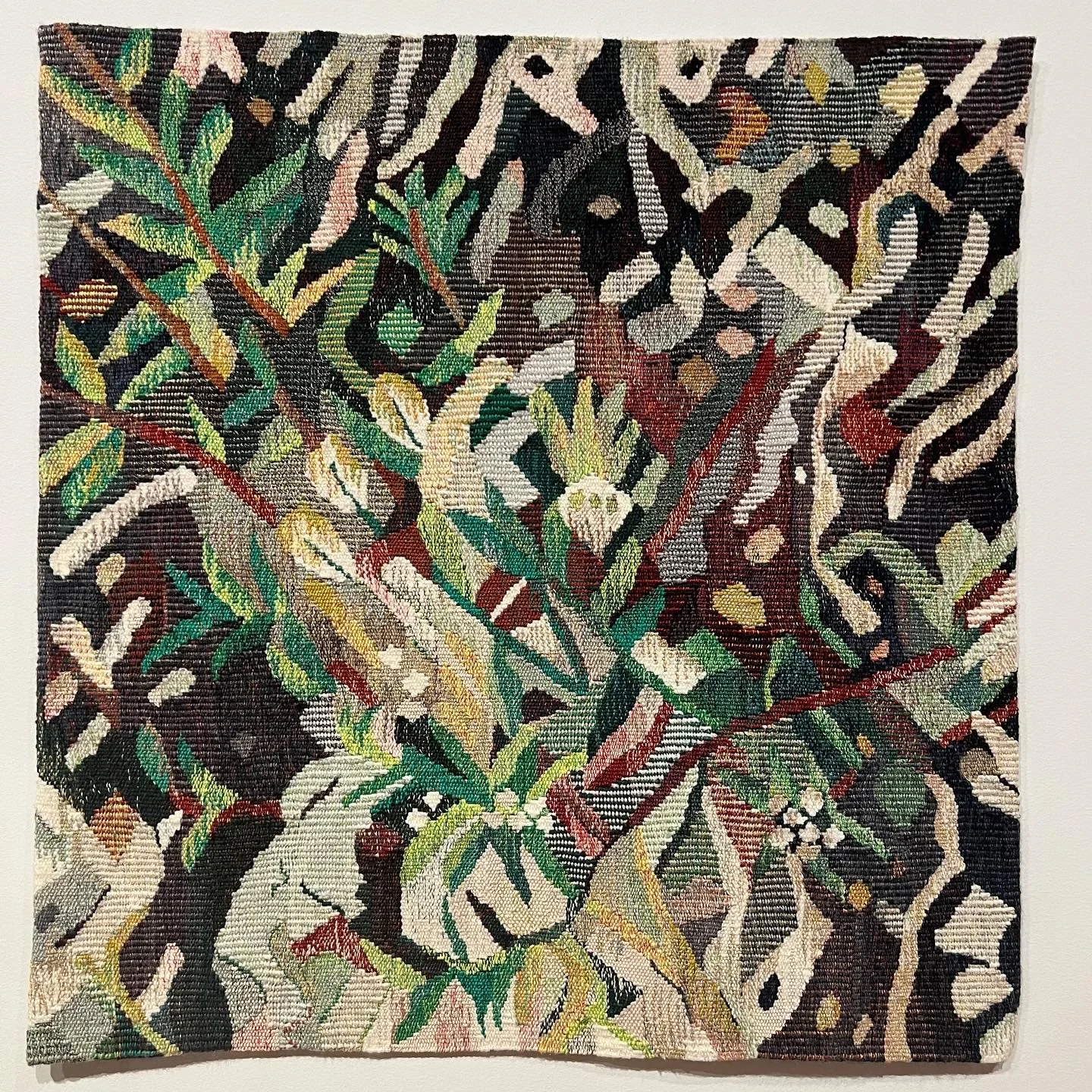 A colorful woven tapestry piece with various plant and floral patterns in green, yellow, beige, and black tones.