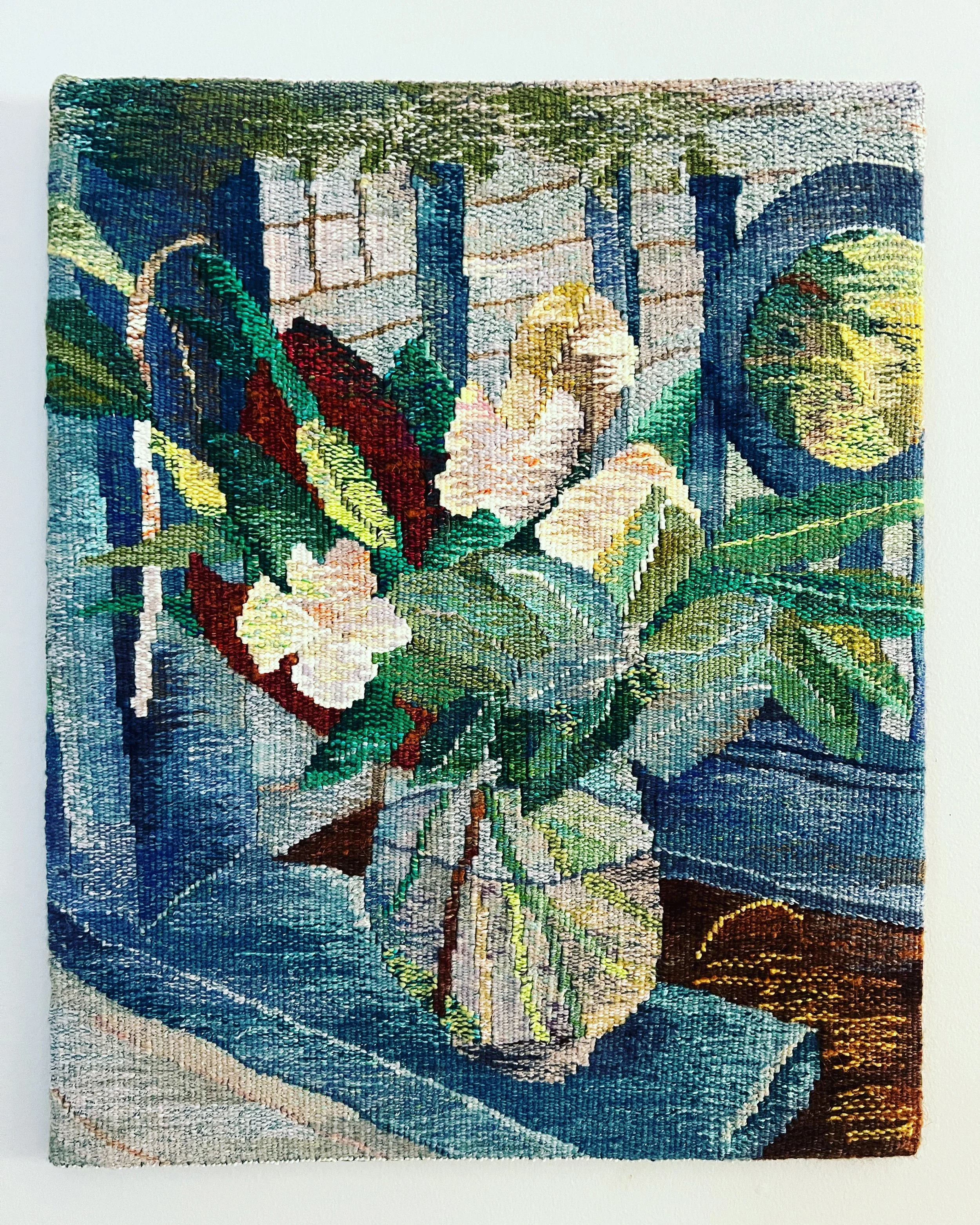 A colorful woven tapestry depicting a vase of flowers left on a doorstep.