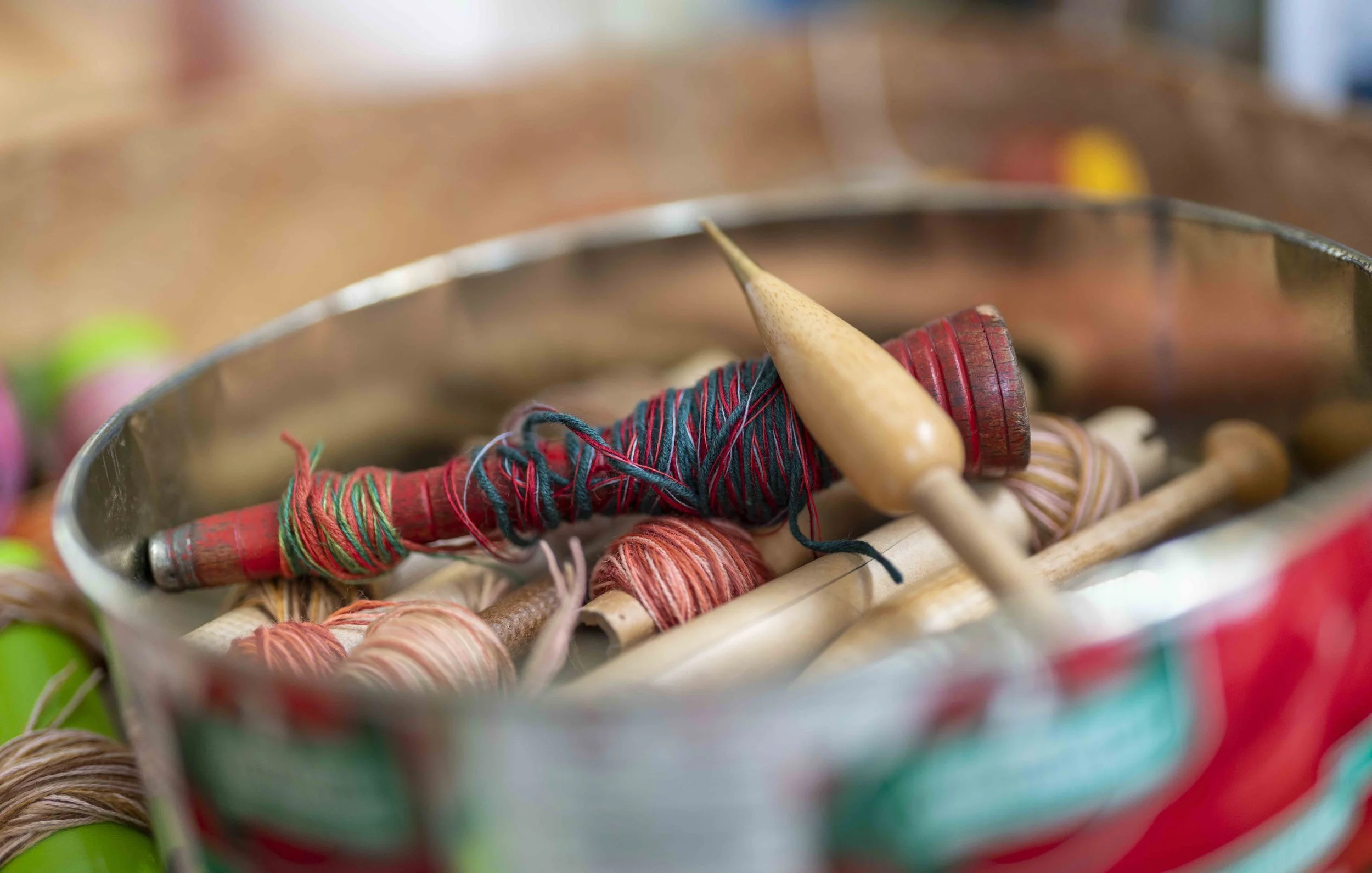 Close-up of colorful yarns and wooden tapestry bobbin in a container.
