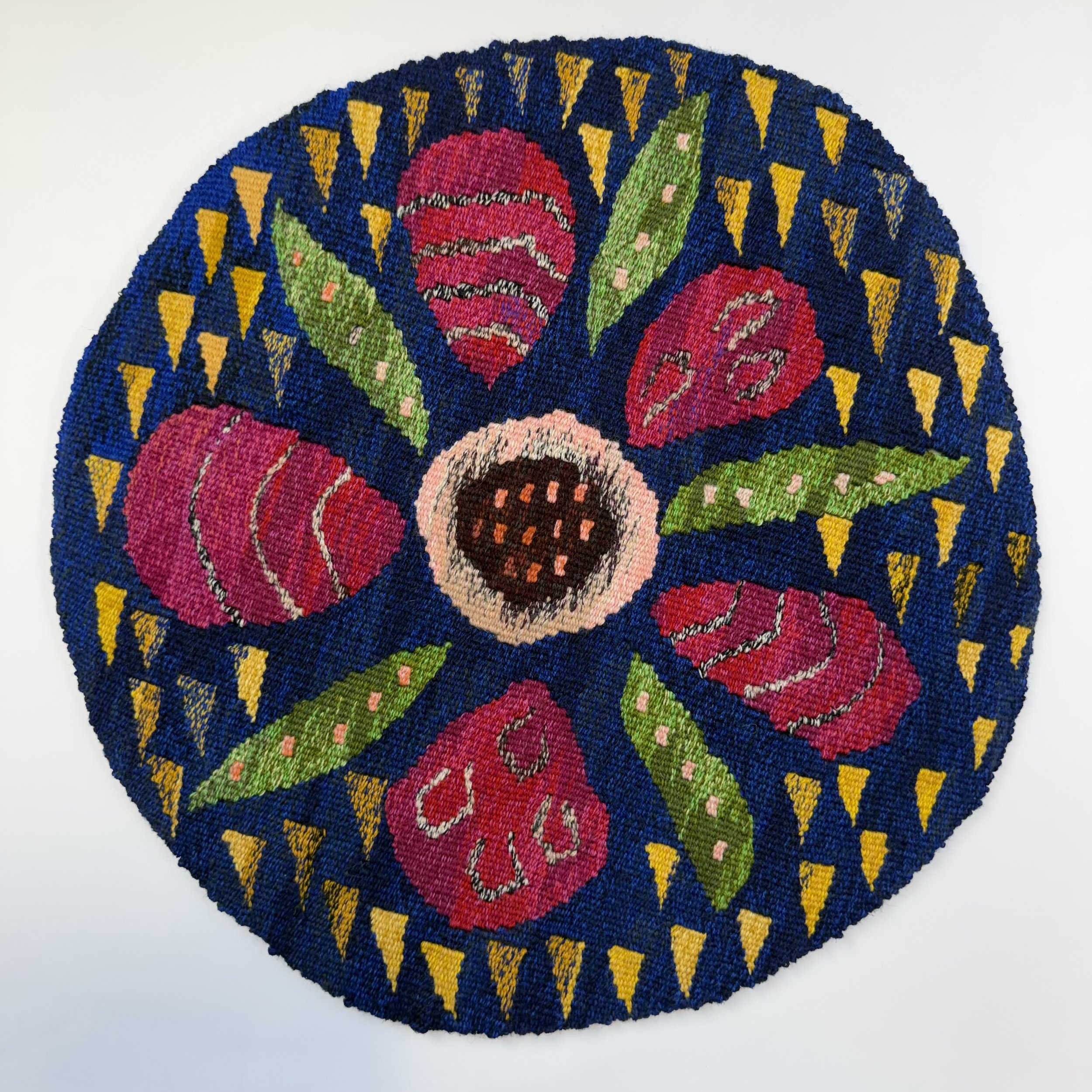 Colorful embroidered circular piece with red roses, green leaves, and yellow accents on a dark blue background.