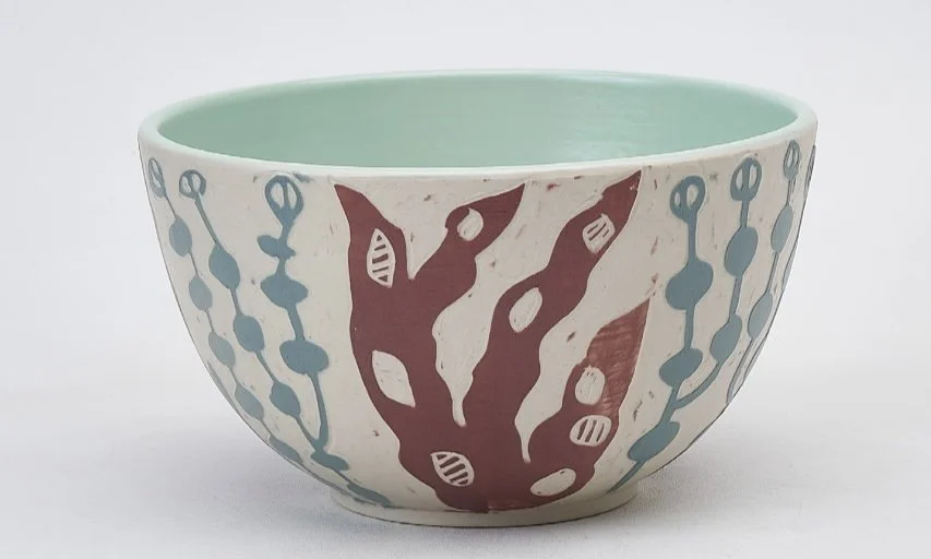 Dimity Kidston sgraffito hand carved ceramic plate with a light green interior, decorated with abstract red and blue patterns on a white background.