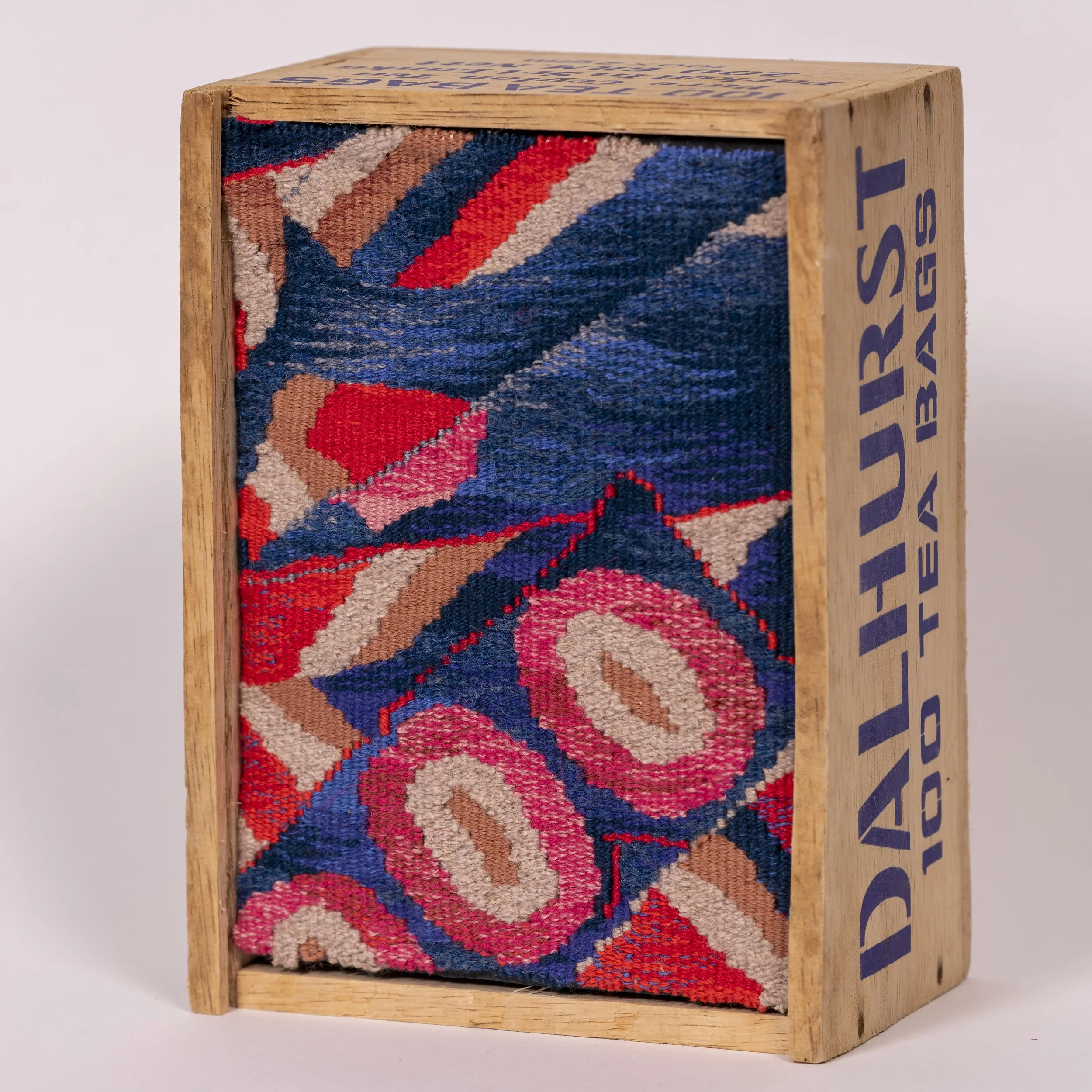 Close-up of a wooden frame with a colorful woven textile inside, featuring a floral pattern with pink, red, blue, gray, and beige colors.