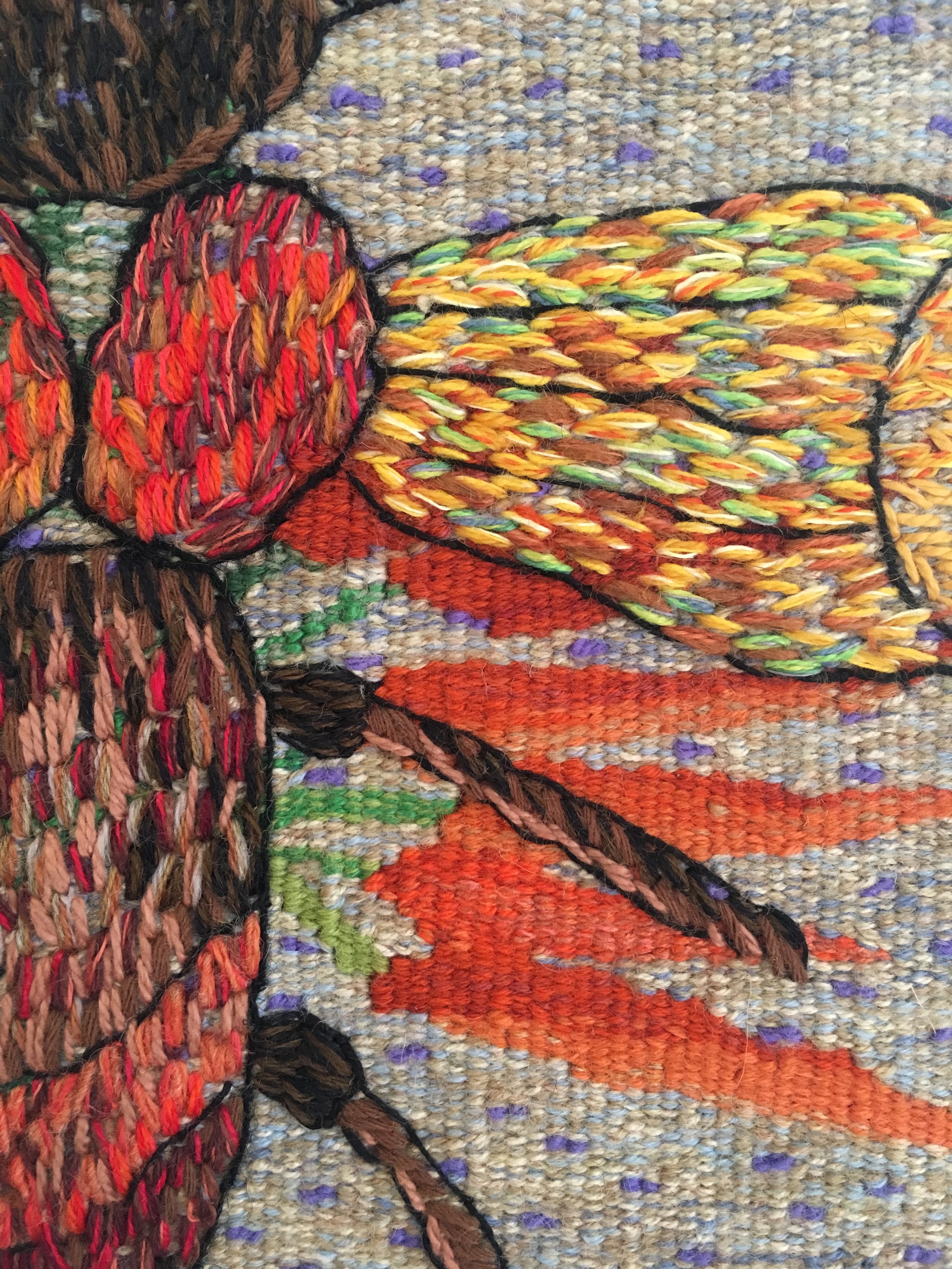Close-up view of a colorful woven textile artwork featuring a geometric pattern with vibrant colors, including orange, yellow, green, and purple, with black outlining.