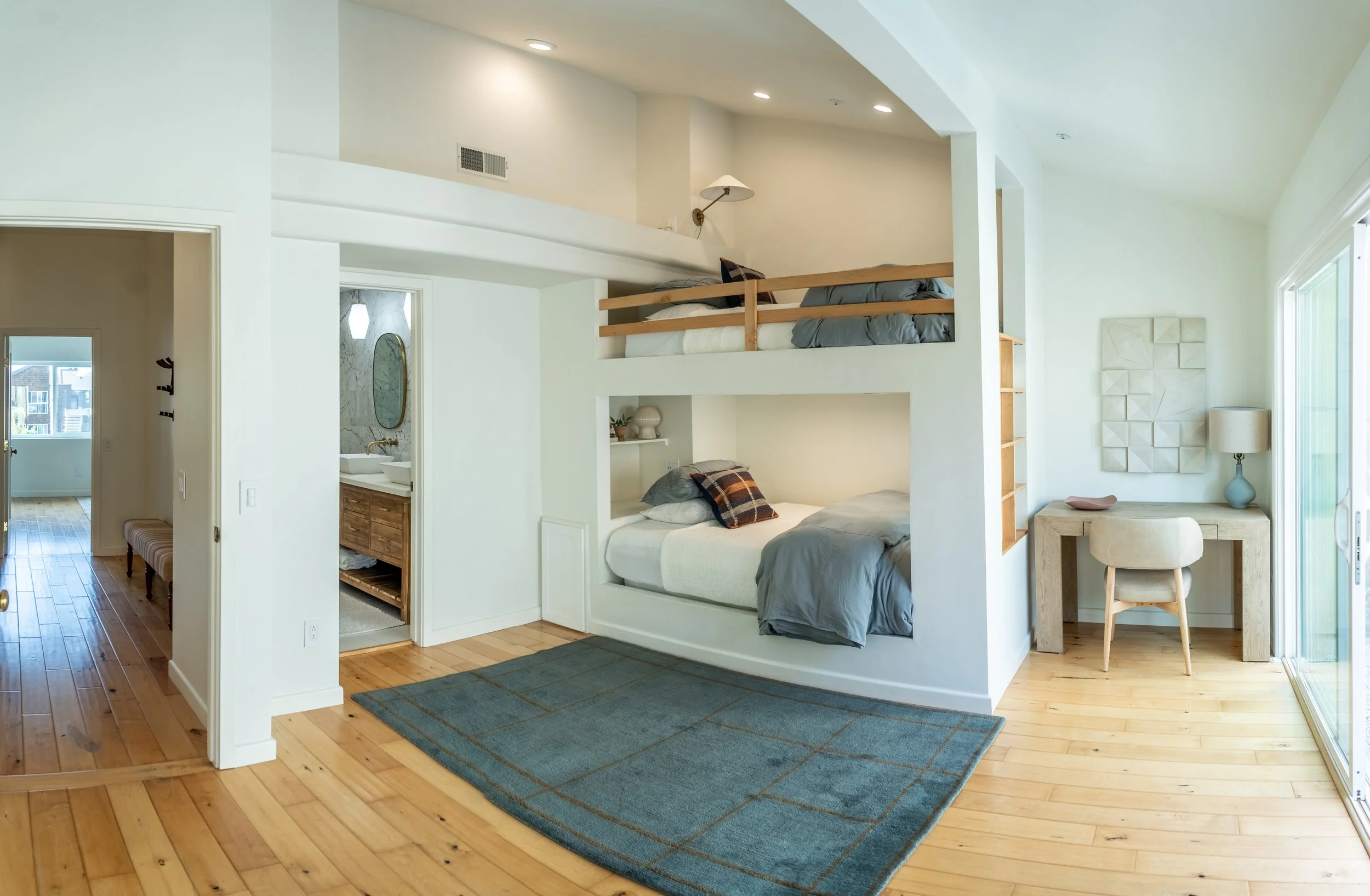Bright bunk room at The Solana House featuring two full-size built-in bunks, a dedicated desk, natural wood floors, and coastal-inspired decor