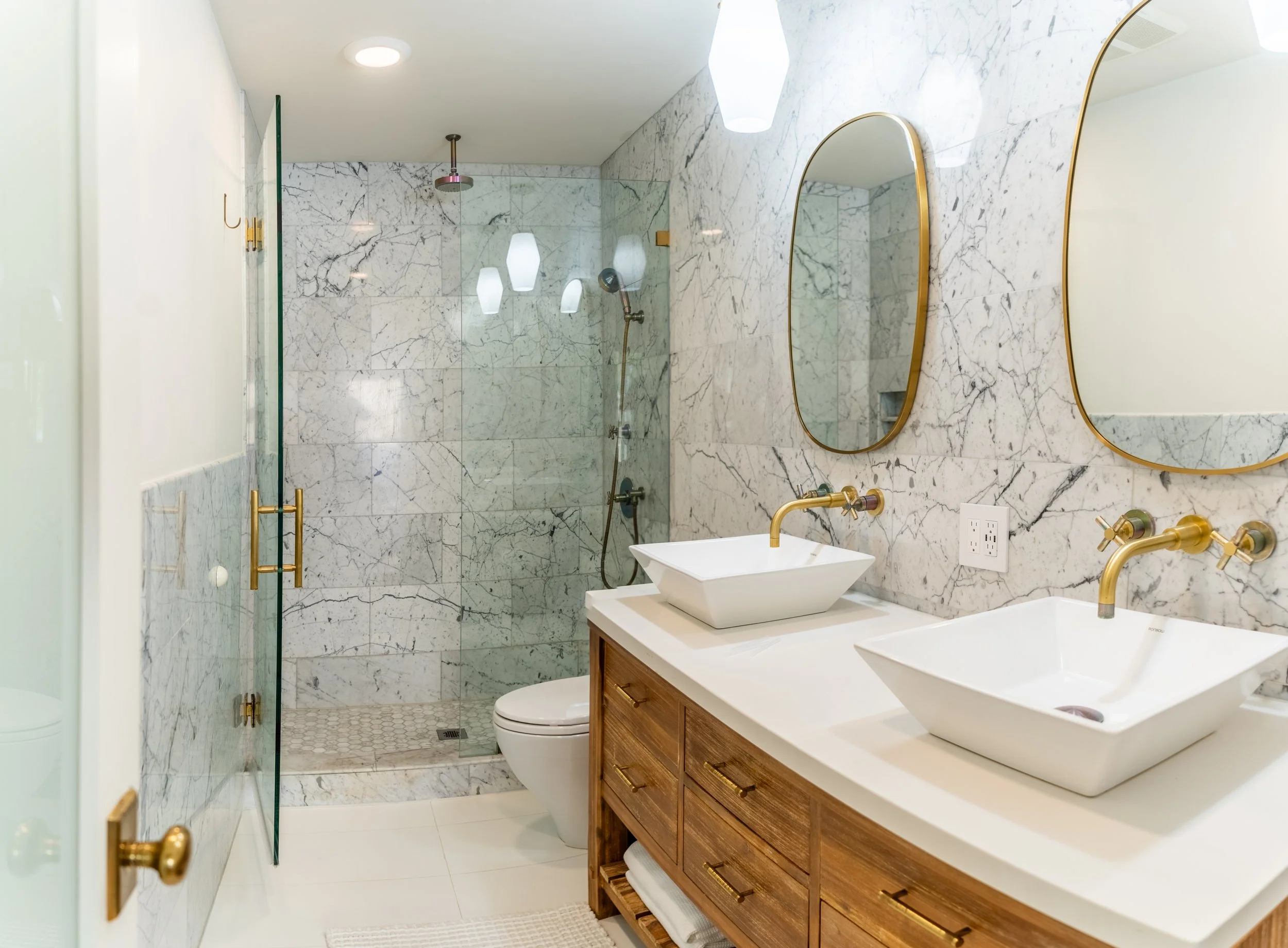 Spa-Inspired bathroom at The Solana House in Solana Beach, California, featuring a double vanity, marble shower, and warm brass fixtures
