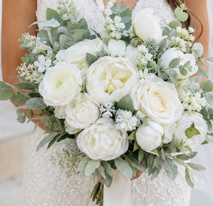 A bride holding a large bouquet of white roses, peonies, and greenery at a wedding.