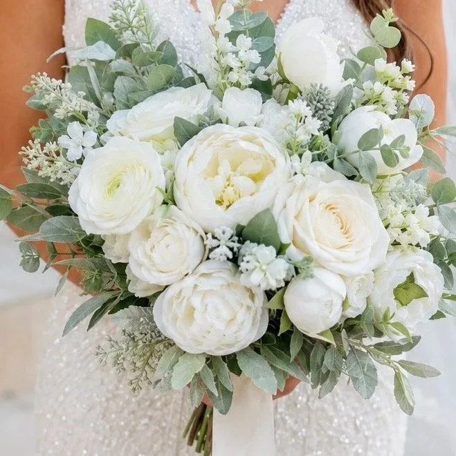 A bridal bouquet with white roses, ranunculus, peonies, and greenery.