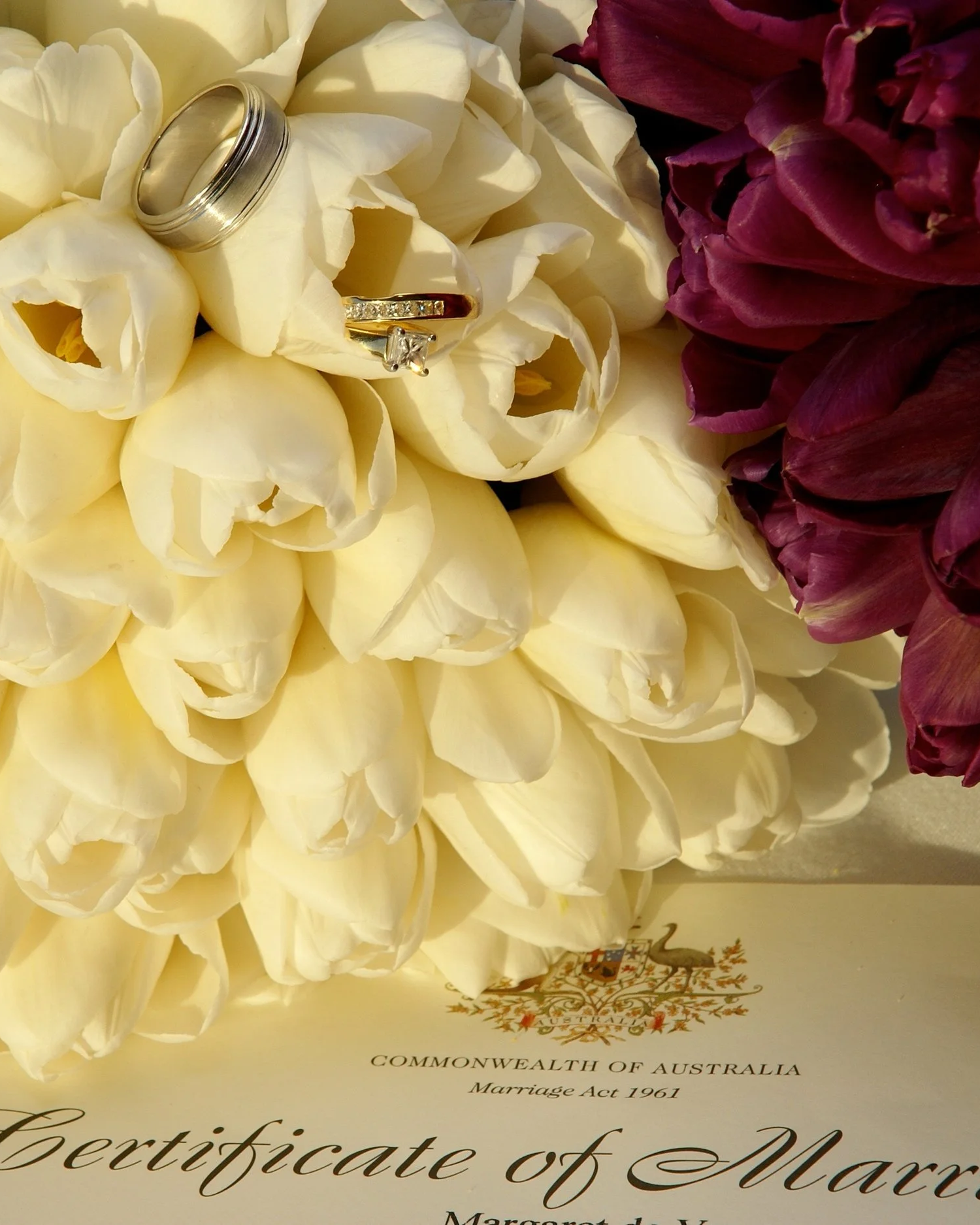 Close-up of white and purple flowers with wedding rings on top, and a marriage certificate from Australia underneath.