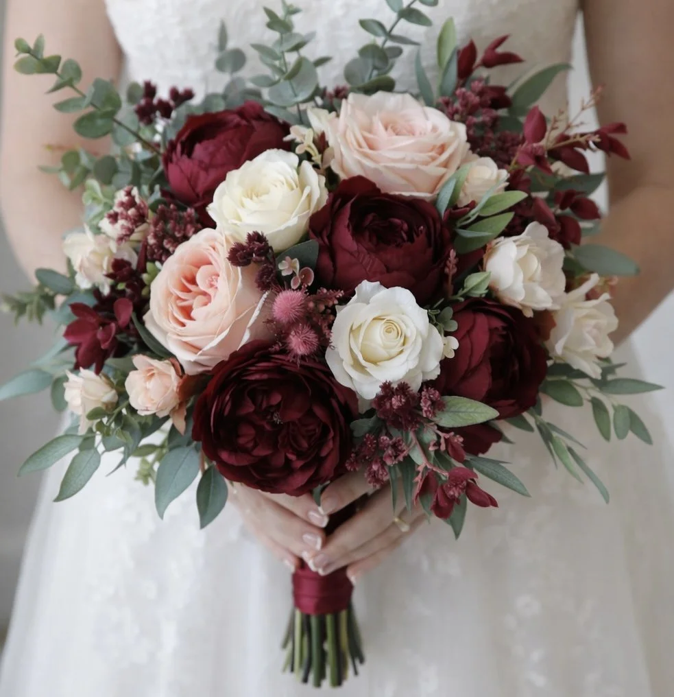 A bride holding a bouquet of red, white, and blush pink flowers with greenery.