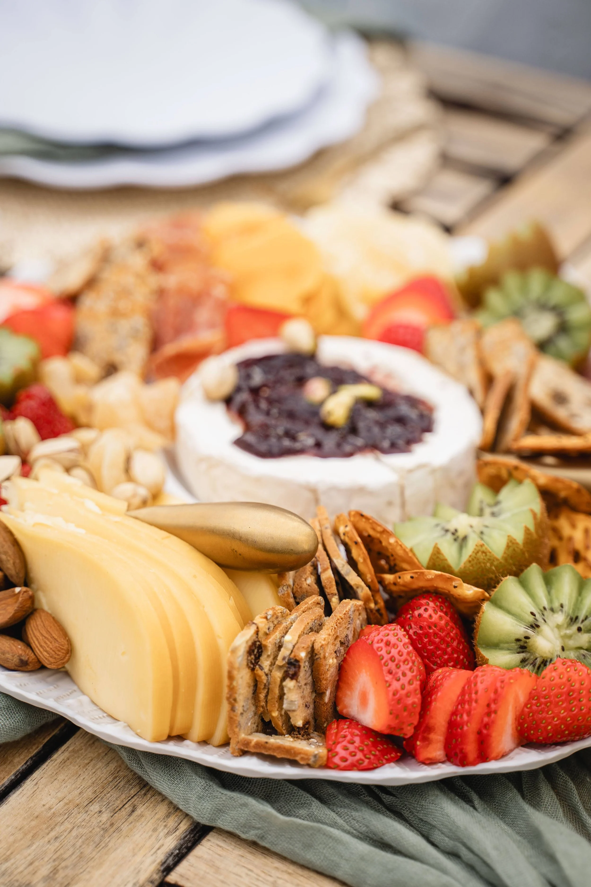 Assorted cheese, strawberries, kiwi, and other fruits on a platter. A jar of jam also in view.