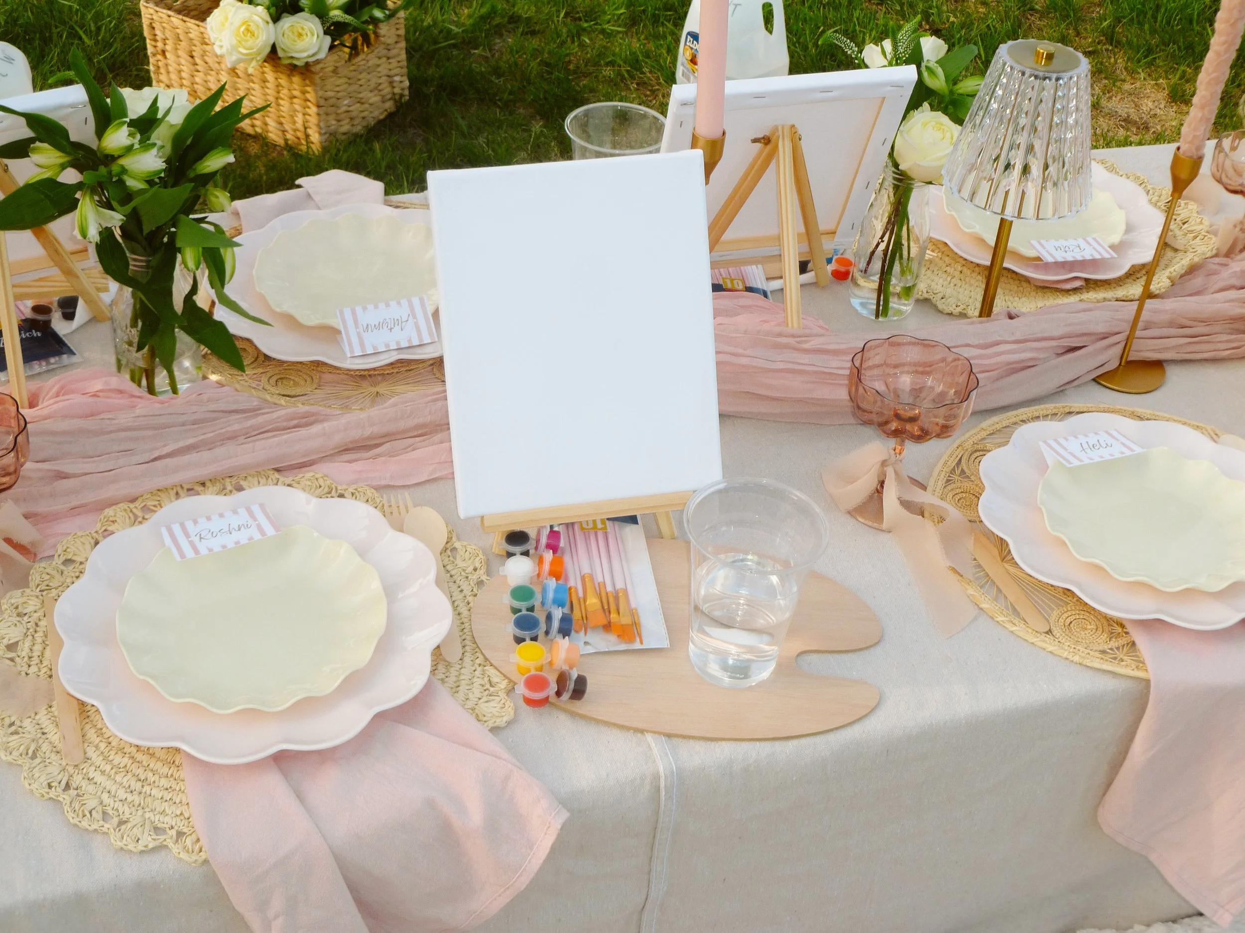 Table decorated with pink and cream linens, surrounded by plates, flowers, candles, and art supplies.