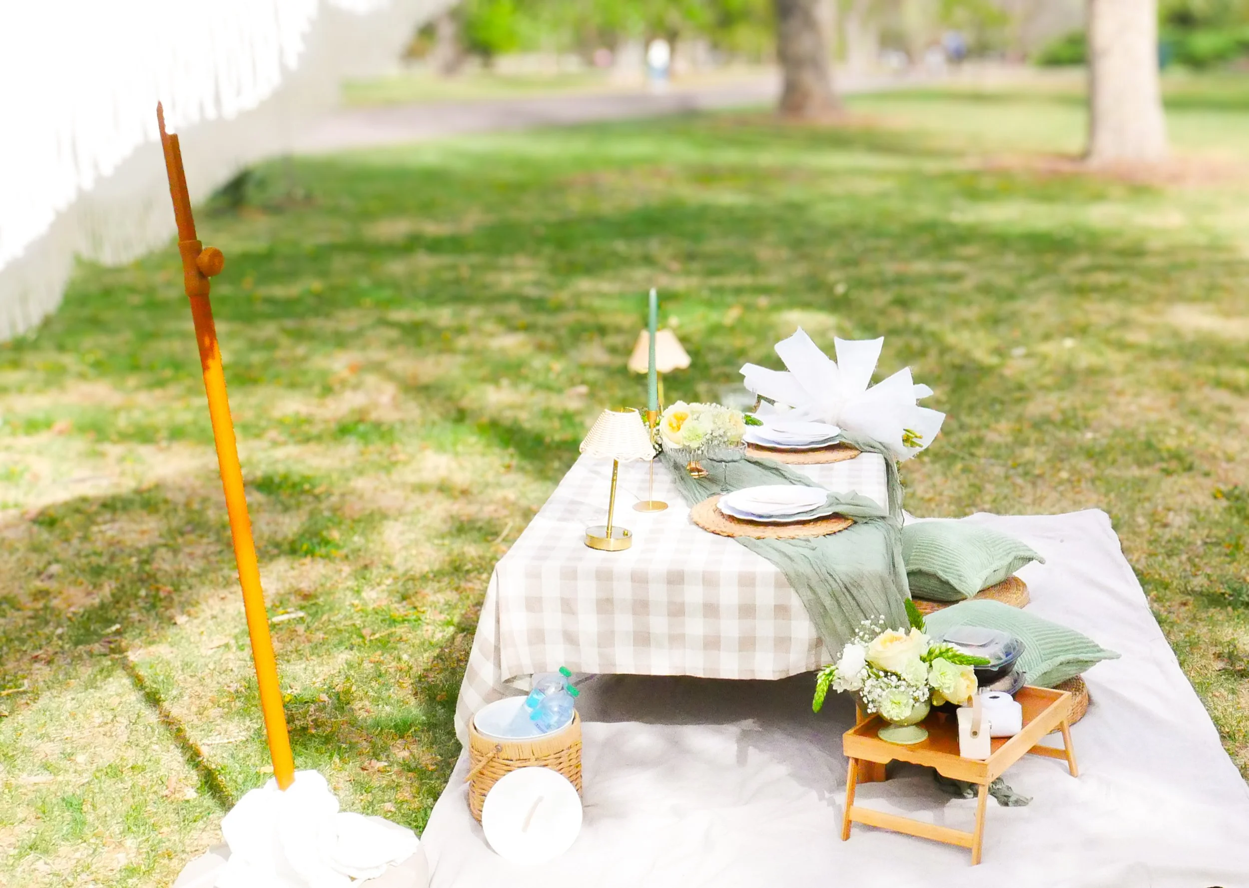 A decorated outdoor table with plates, flowers, and small decorations set up on a grassy area with trees in the background.