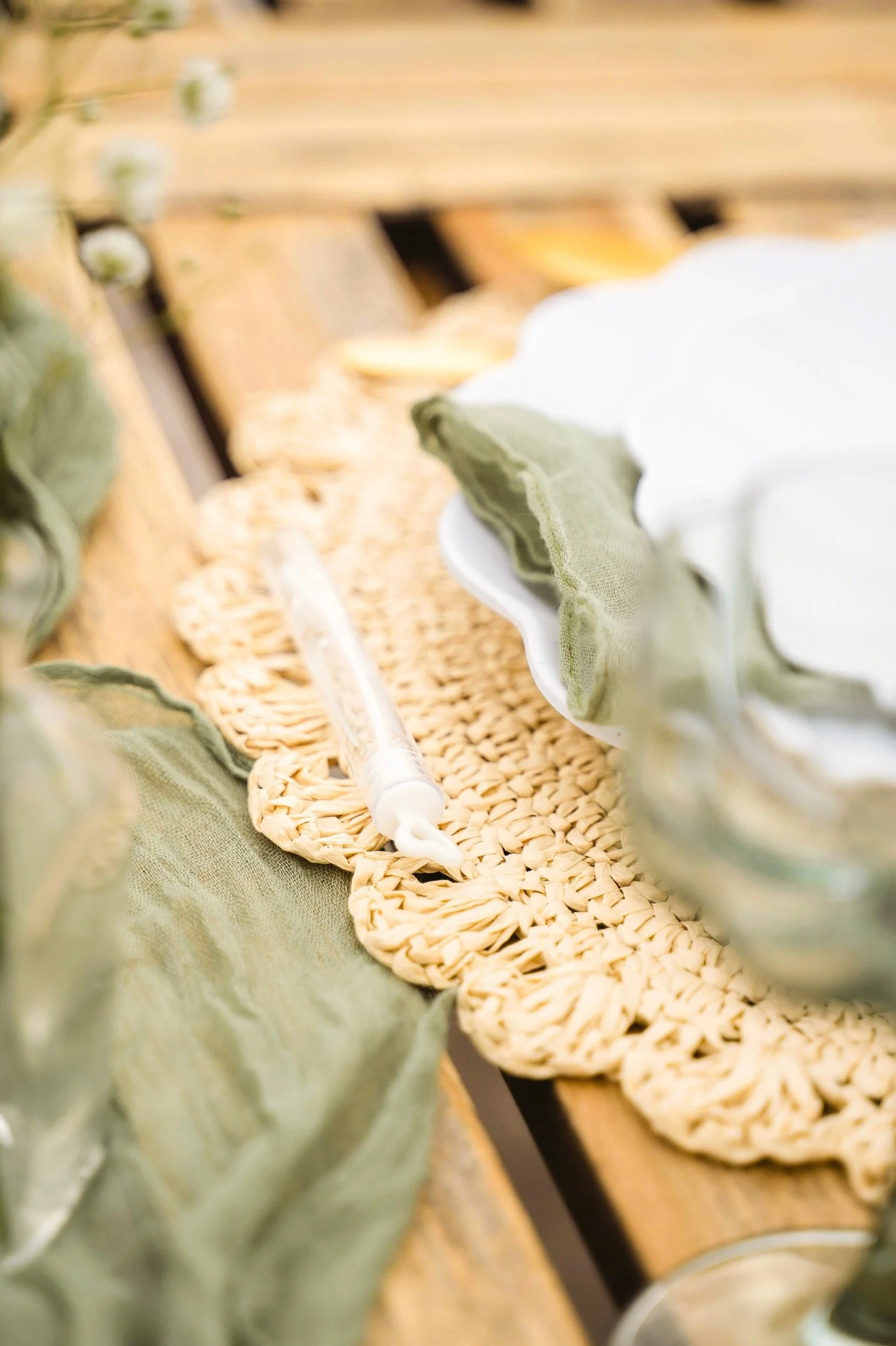 A close-up of a wicker tray filled with uncooked pasta, a white plate with green napkins, and a clear syringe-like object on a wooden surface.