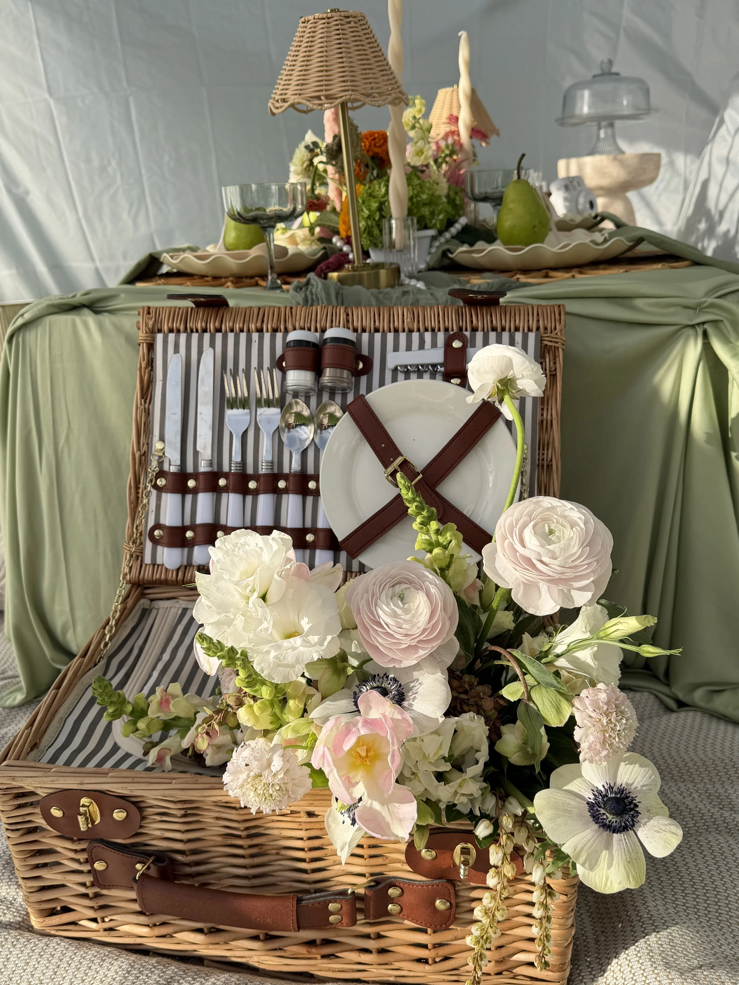 A wicker picnic basket filled with white and pink flowers.