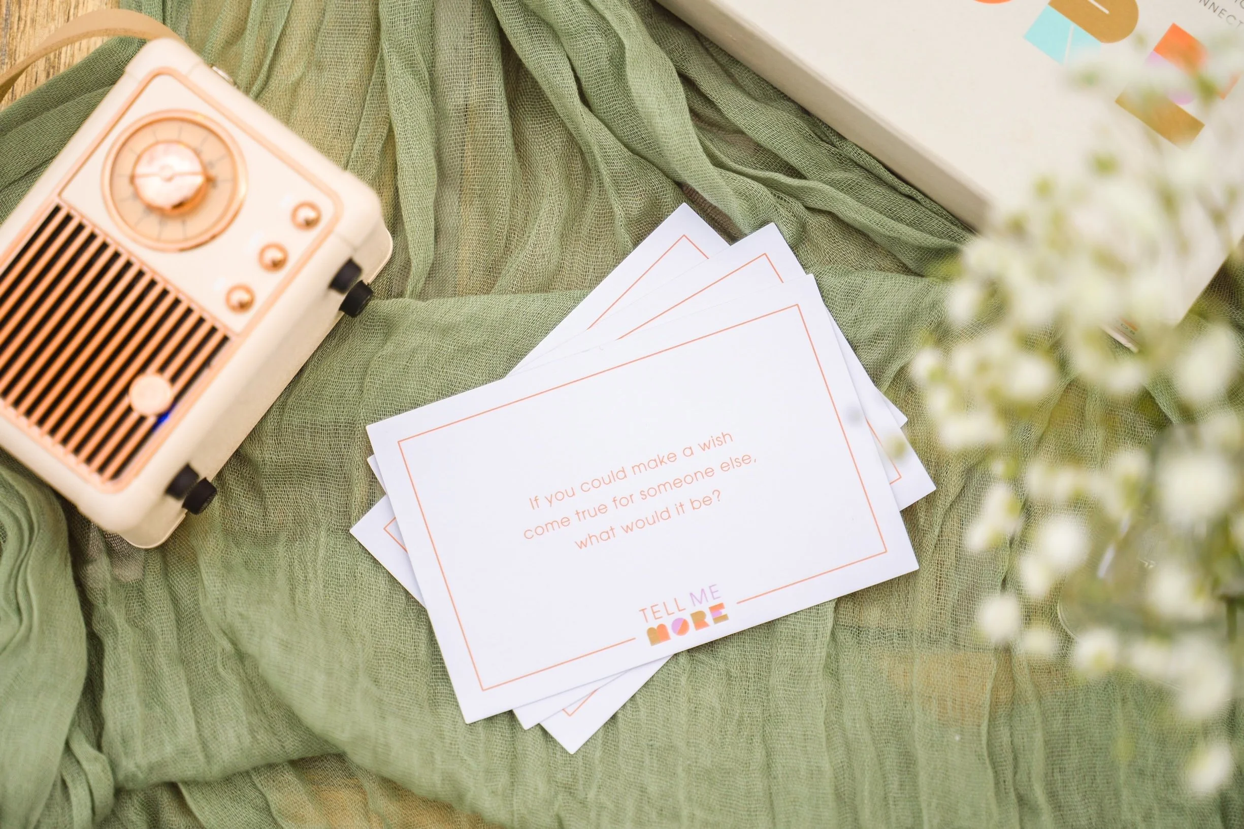 A vintage radio, several flashcards with questions, green fabric, a white box with colorful letters, and a bouquet of flowers on a textured green surface.