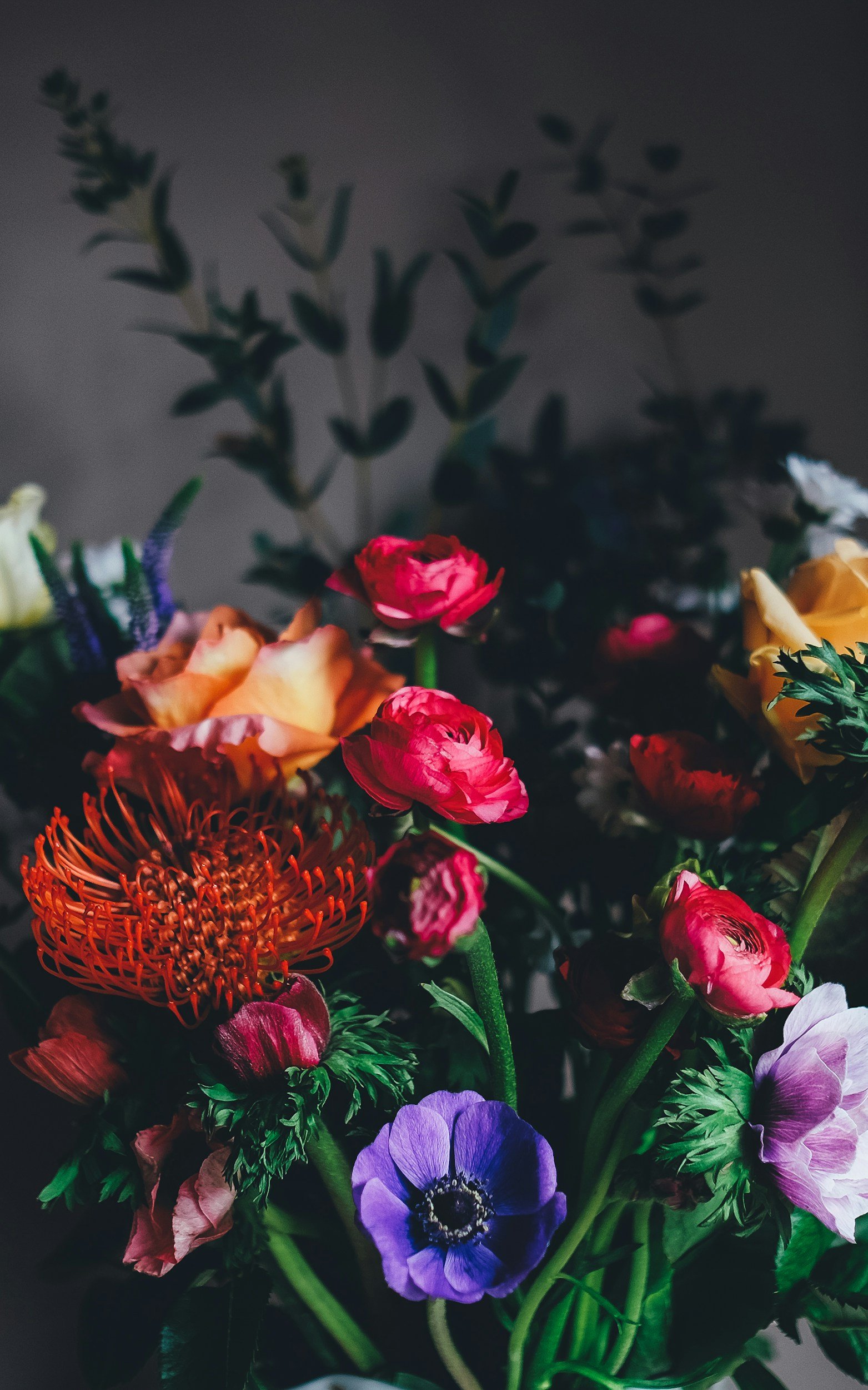 A close-up of a colorful bouquet of flowers with pink, orange, purple, and white blossoms against a dark background.