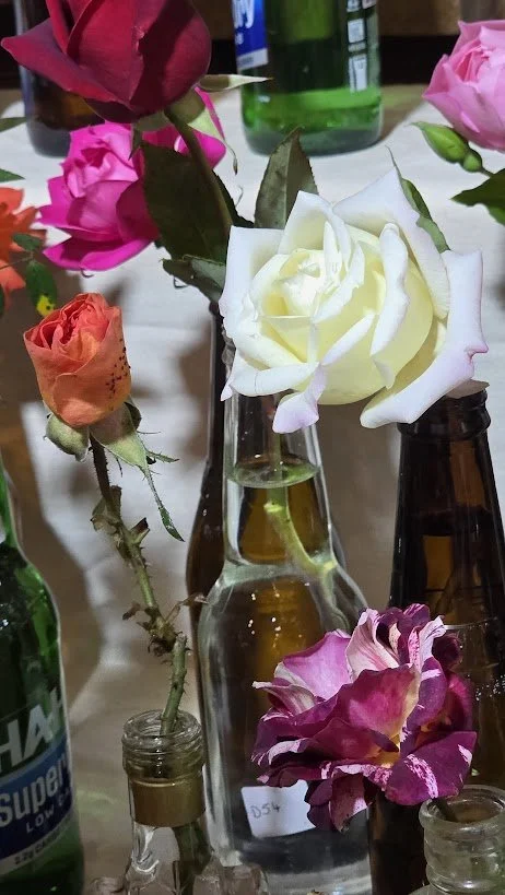 Assorted roses in glass bottles on a table, including white, pink, orange, and purple roses.