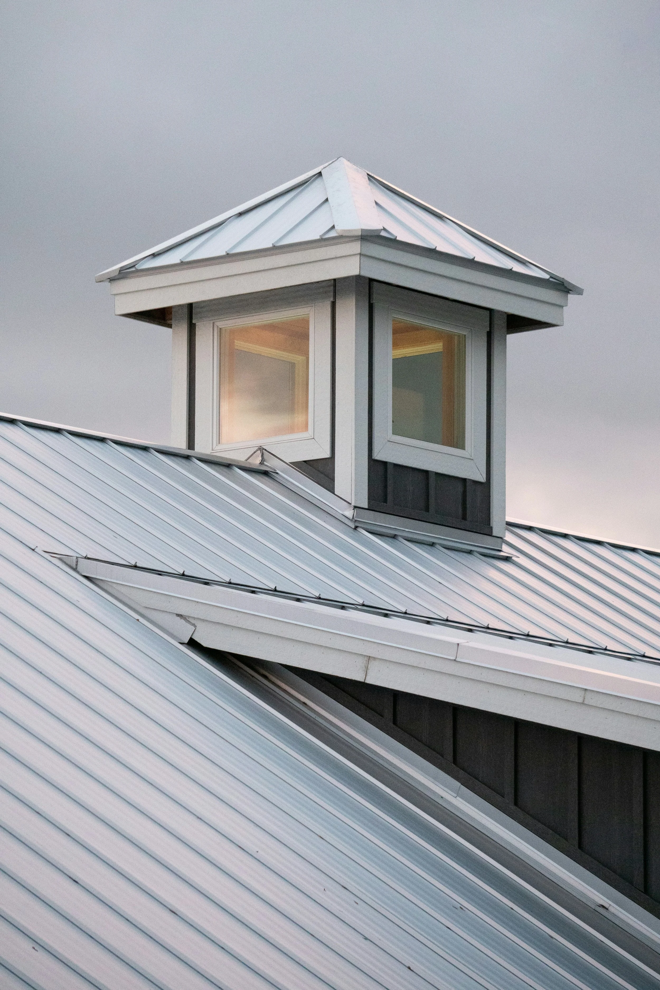 Close-up view of a small dormer window with a metal roof on a modern house, under a cloudy sky.