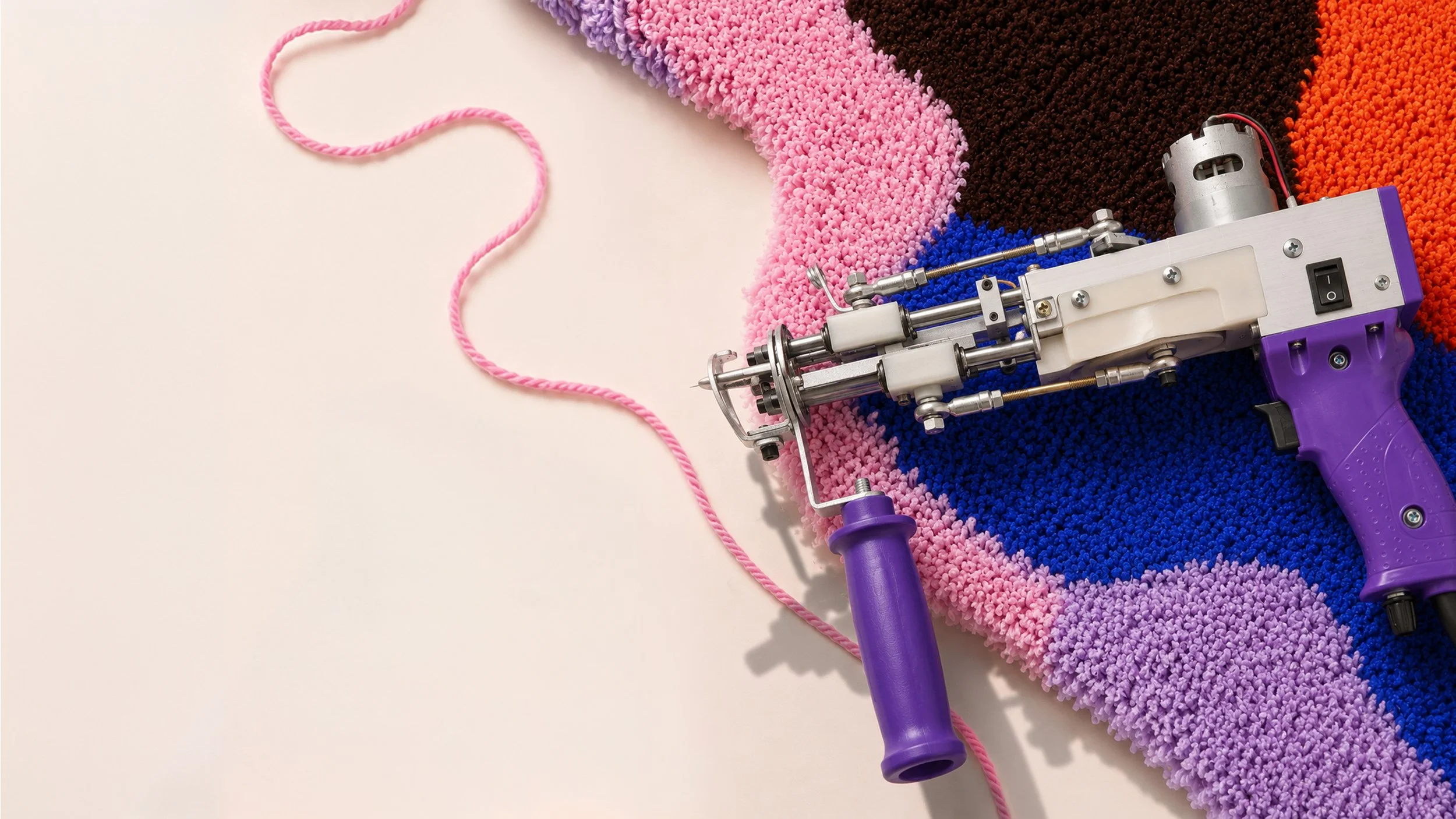 Ein Teppich aus bunten, weichen Pompons in Farben wie Pink, Lila, Blau, Schwarz und Orange. Darauf liegt ein Pulver-Strahler mit einem pinken Seil