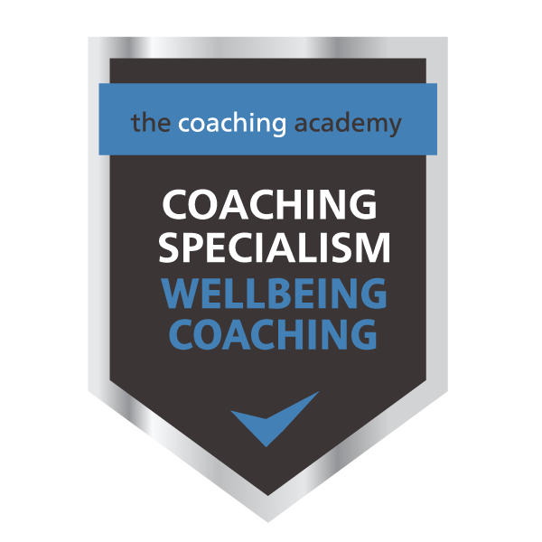 A badge with a silver top, dark background, and blue accents displaying the text 'the coaching academy,' 'COACHING SPECIALISM,' and 'WELLBEING COACHING,' with a blue checkmark at the bottom.