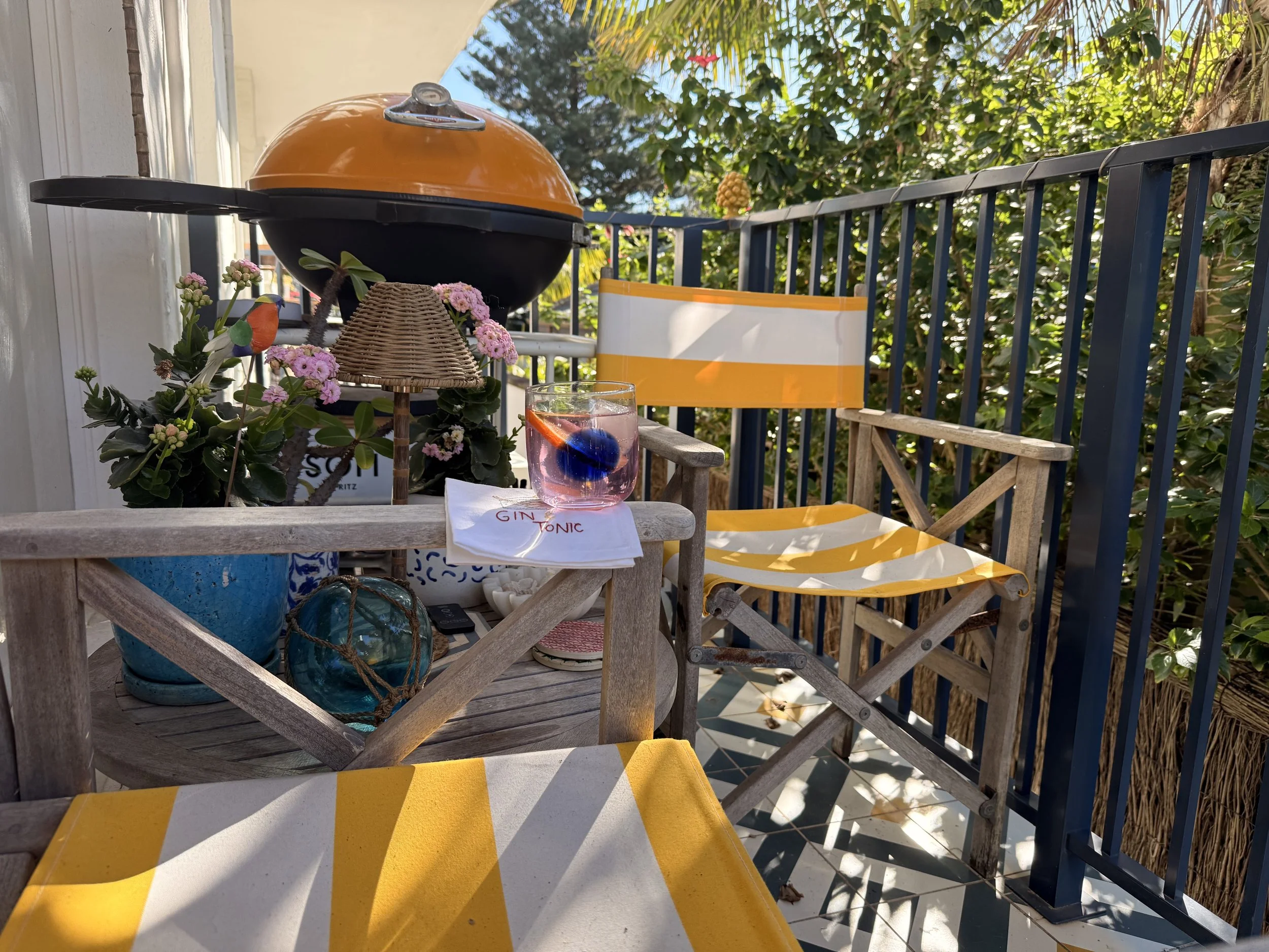 Sea Fan balcony set up for a relaxed barbecue, with the BBQ, yellow-striped chairs, flowers and a Sea Fan Sunset drink.