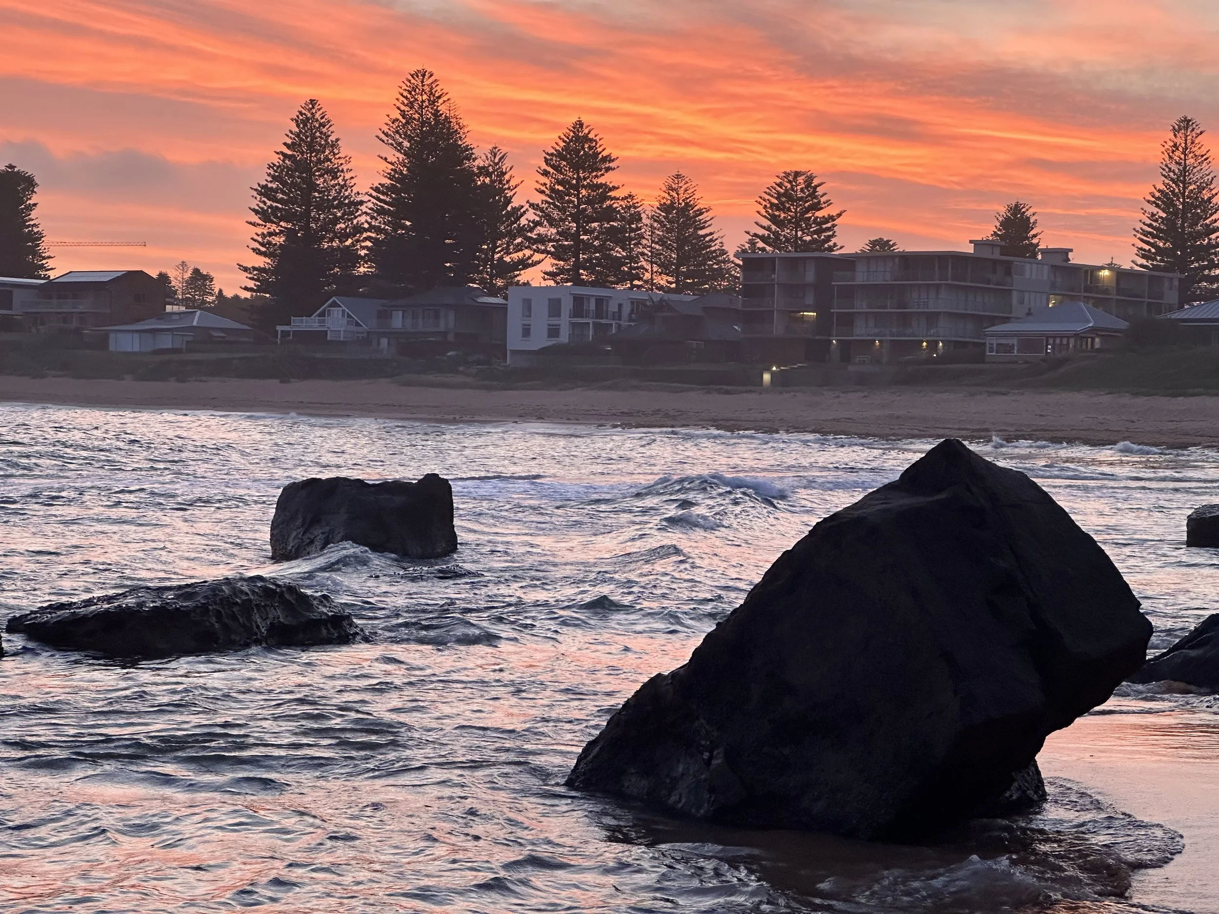 Pink sunset over the Basin at Mona Vale Beach, viewed across the water and rock formations toward Sea Fan at Thirteen Surfview Road
