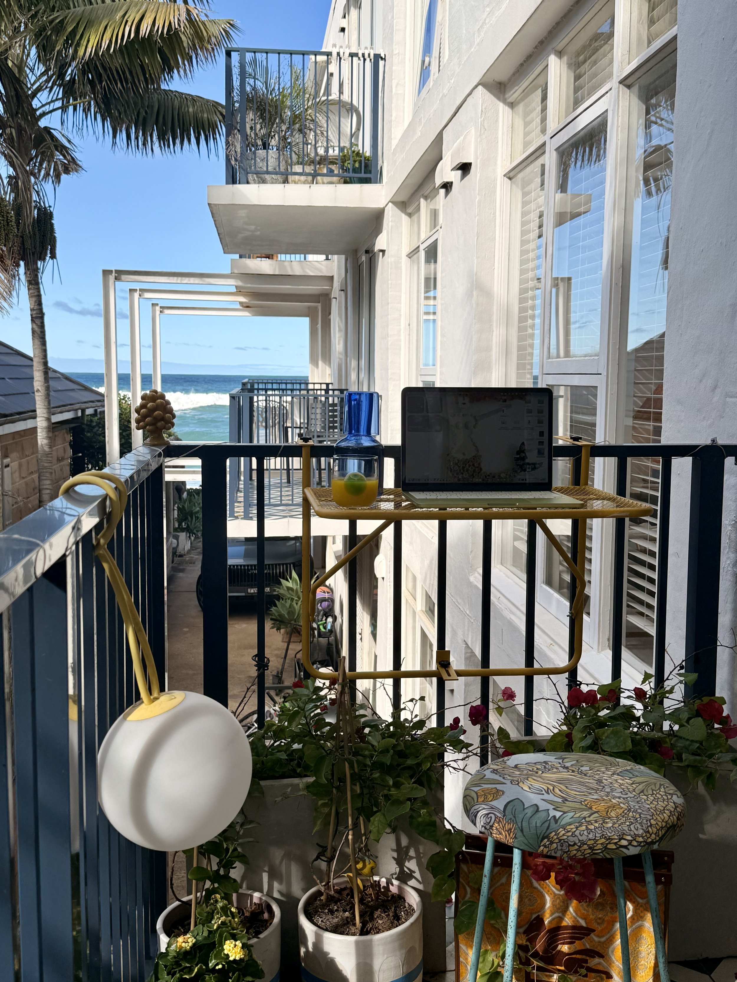 Laptop workspace on the Sea Fan balcony with ocean views, tropical plants and a colourful stool.