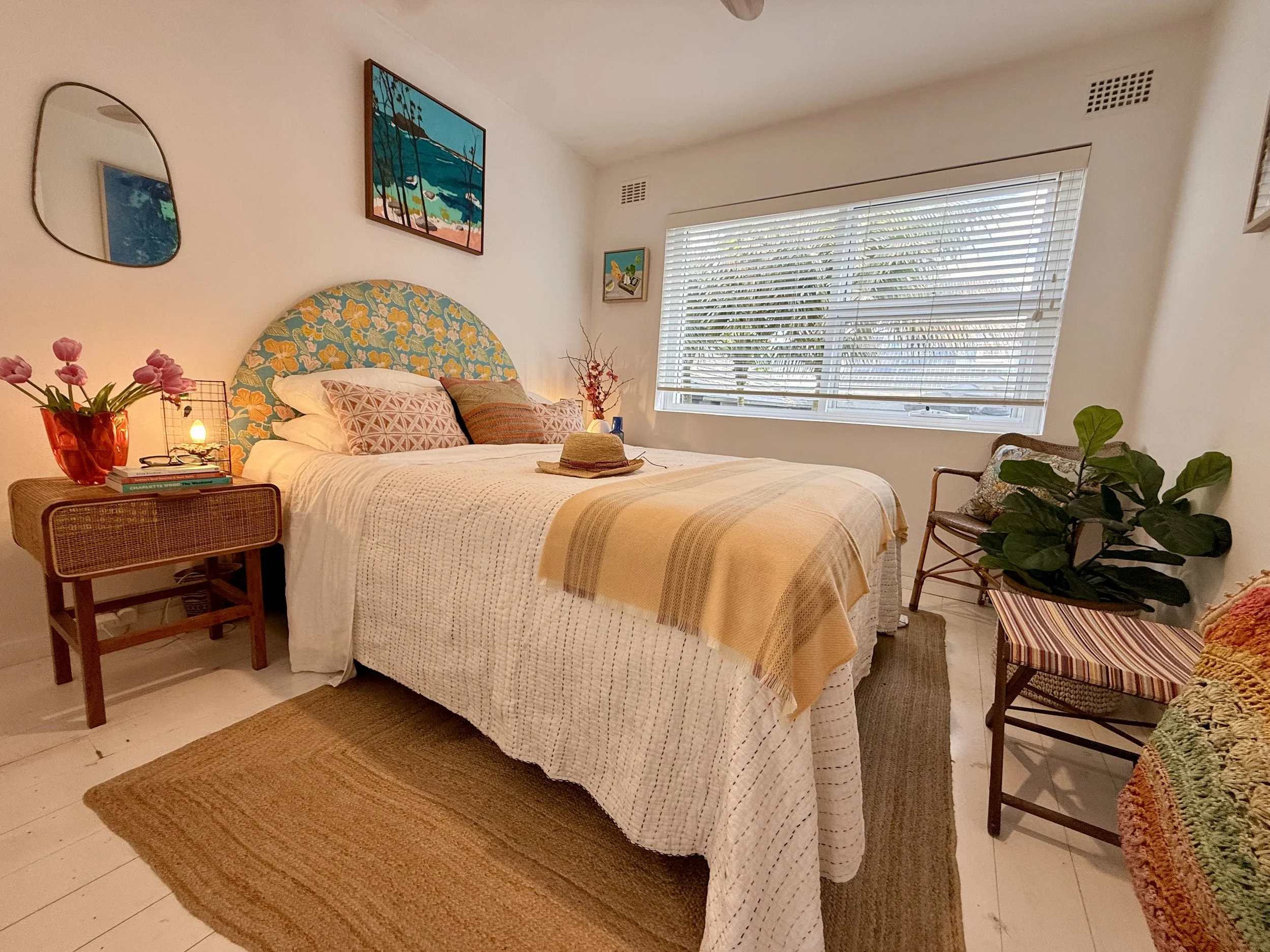 The Basin Room queen bed with a custom Anna Spiro Oahu fabric headboard, white CULTIVER linen, Cullendale Irish wool throw rattan bedside table and Nicola Woodcock Palm Beach from West Head artwork.