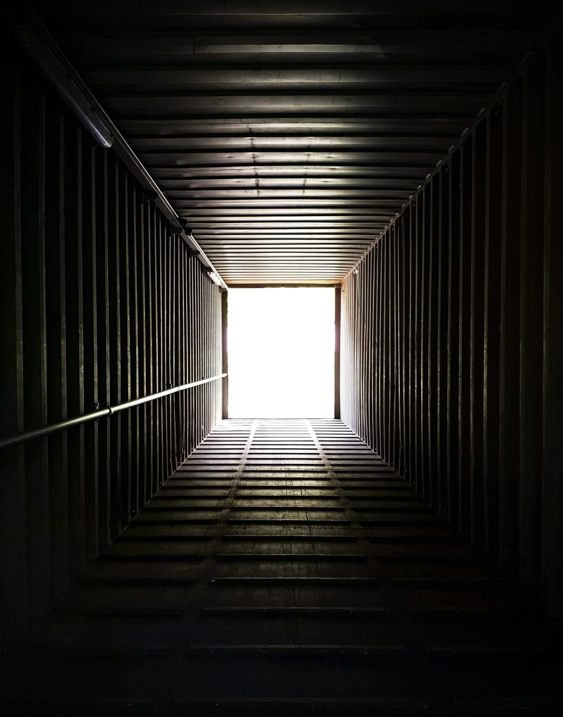 Dark corridor with metal walls and ceiling, leading to bright light at the end.