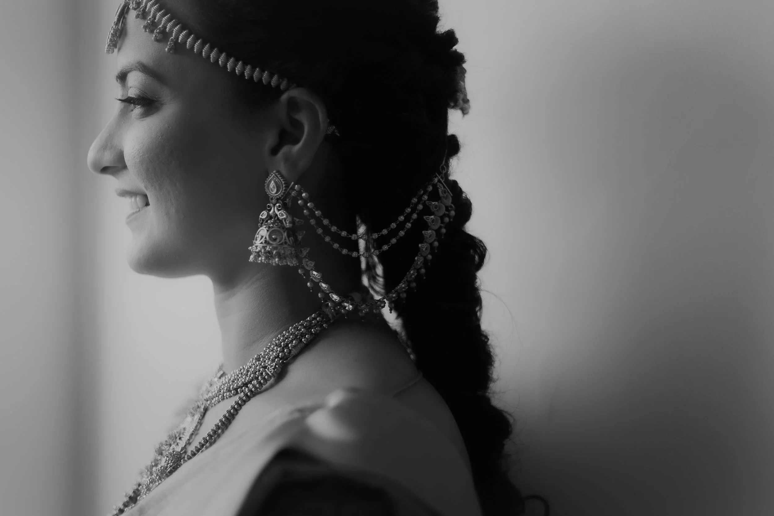 A side profile of a woman with dark skin, wearing intricate jewelry and headbands, in black and white.