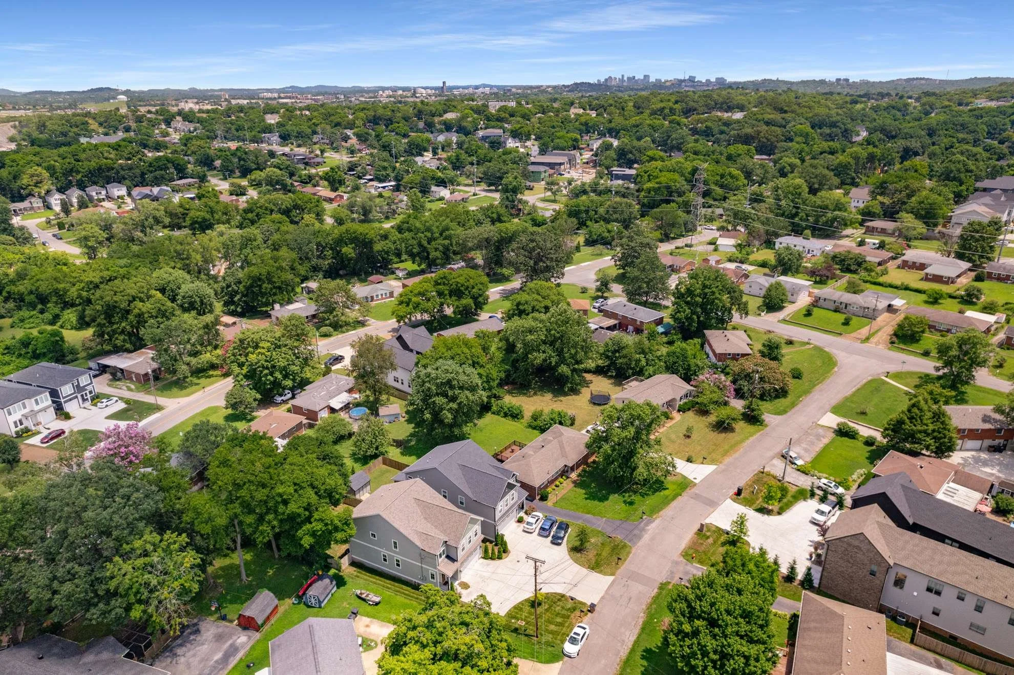 Aerial view of a Tennessee neighborhood with numerous houses, trees, and streets, with a city skyline in the distance under a blue sky.
