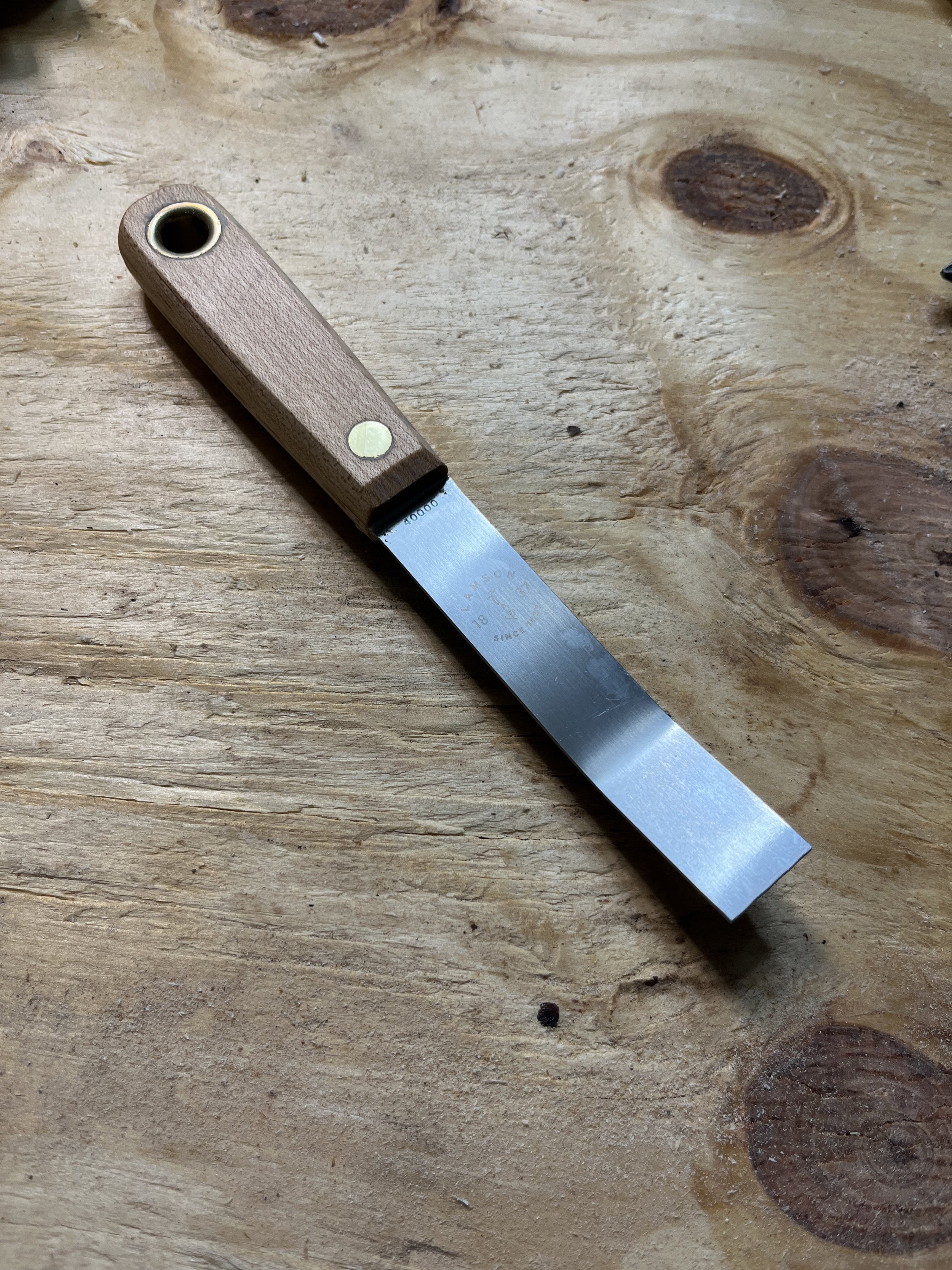 A woodworking hand saw with a wooden handle and metal blade lying on a wooden surface.