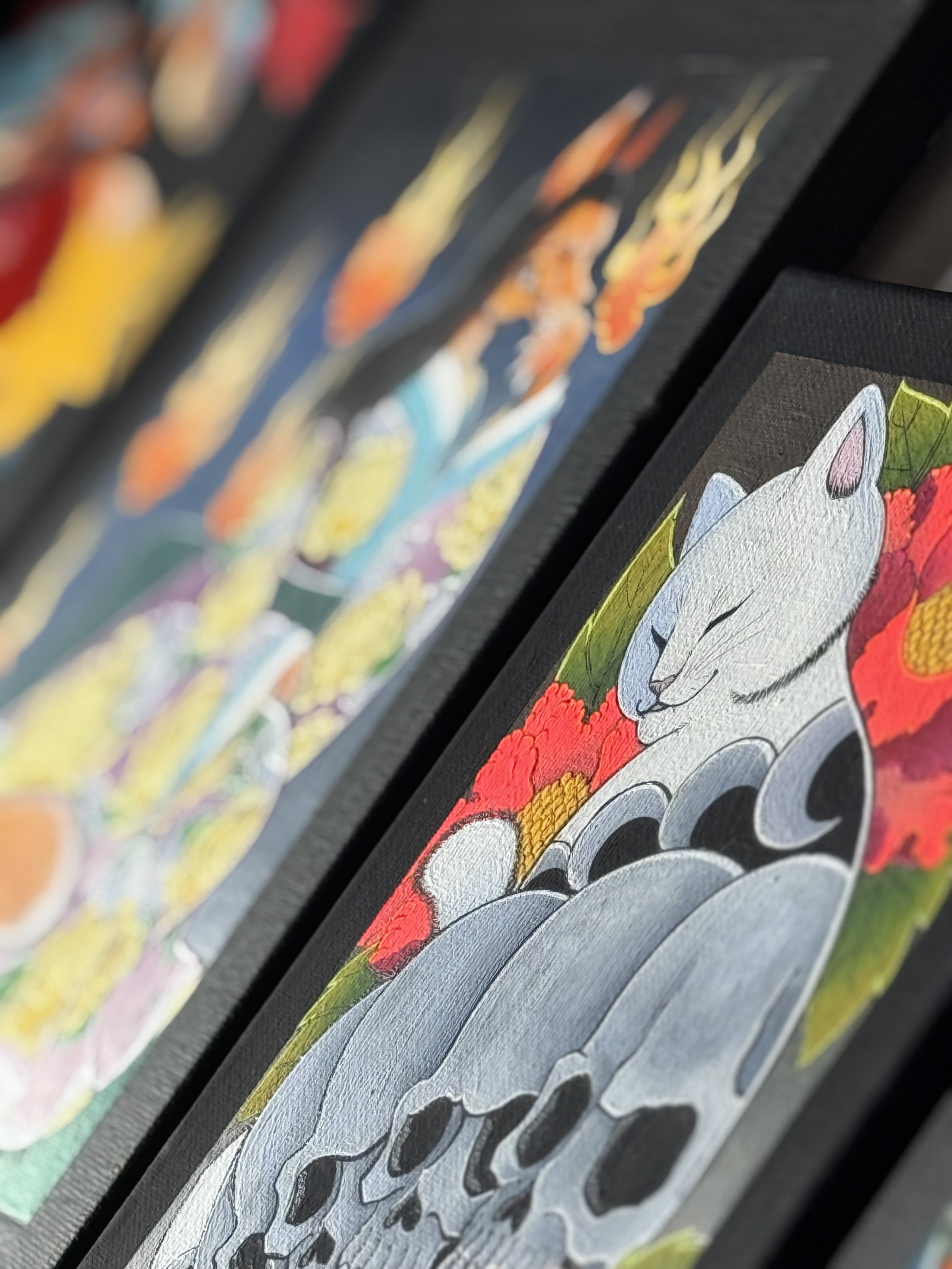 Close-up of a colorful artwork featuring a white cat with repeating skull markings next to another blurred artwork