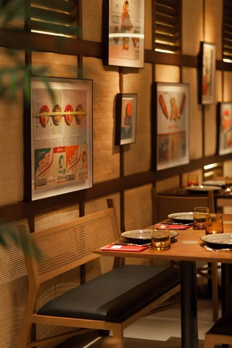Empty restaurant table set with plates, glasses, and red napkins, with a wall decorated with framed artwork in the background.