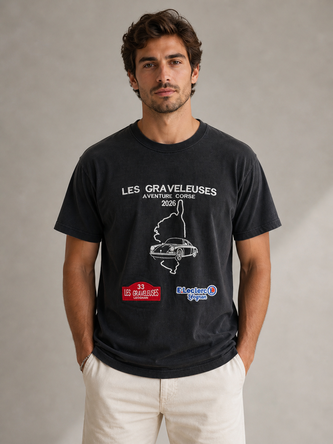 Un jeune homme avec des cheveux bruns, portant un t-shirt noir avec des logos et du texte français, posé contre un fond neutre.