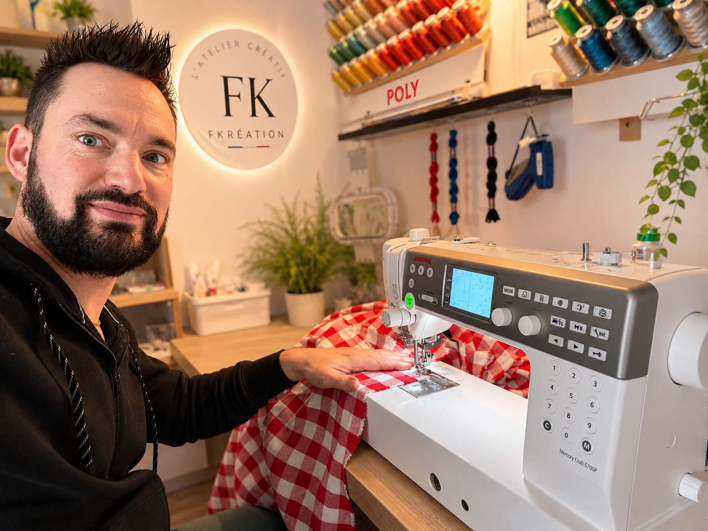 Un homme utilise une machine à coudre dans un atelier de couture, entouré de bobines de fil colorées et de plantes; arrière-plan avec un logo 'FK Création'