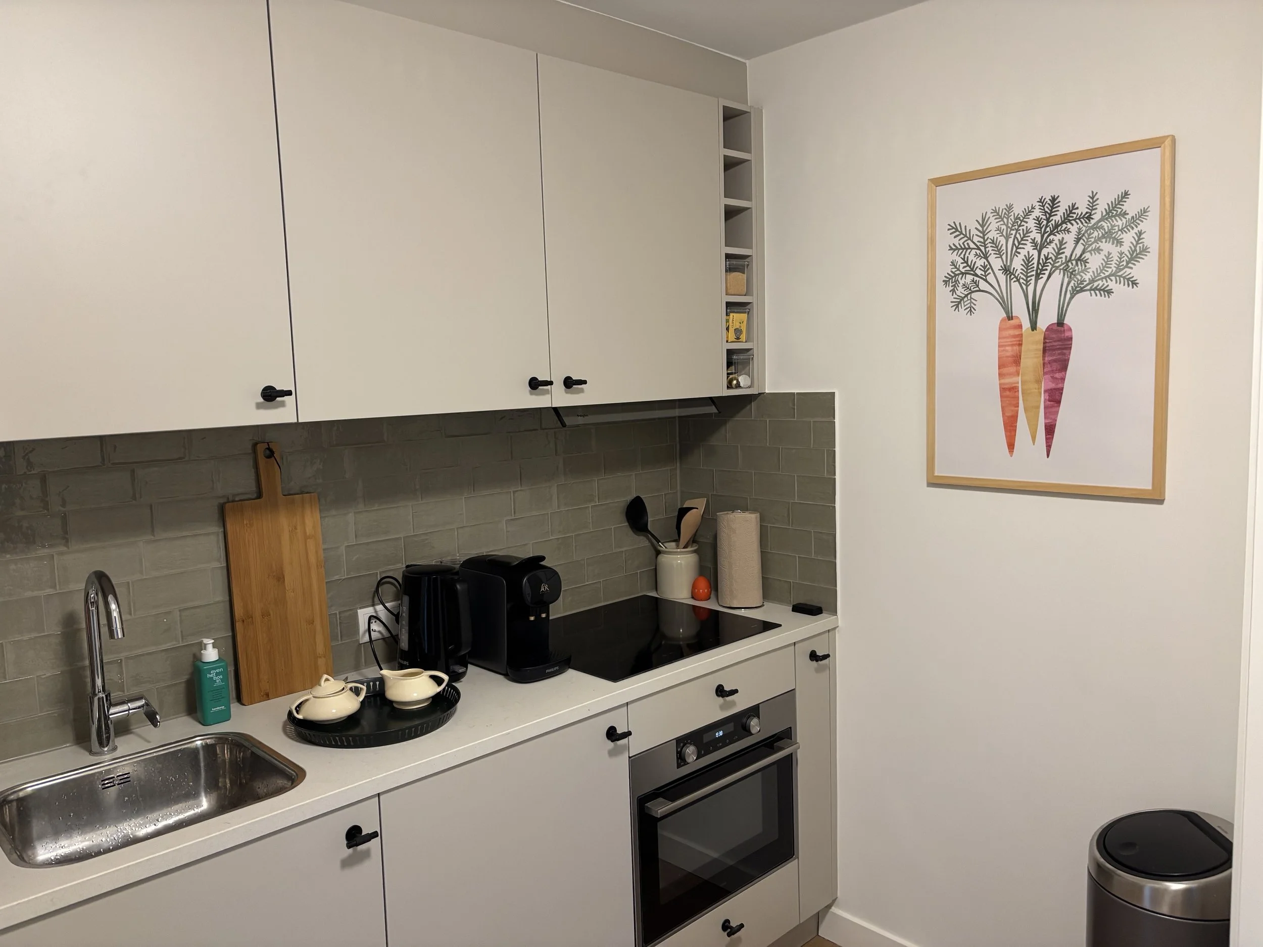Een keuken met witte kasten, een gootsteen, een koffiezetapparaat, en een muurdecoratie met vaze en groene bladeren.