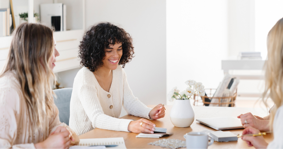 Three women seated at a table sharing ideas with joy and openness – representing trust, confidence, and the Courage Virtue of The Soul Award
