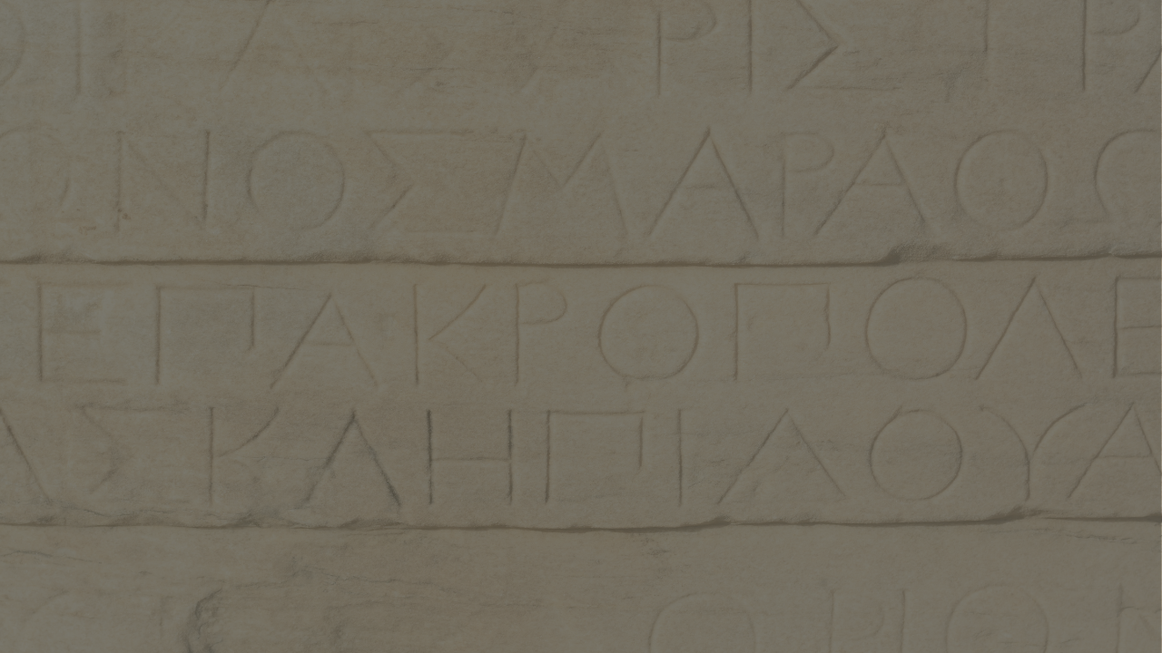 Close-up of an ancient Greek inscription carved into marble, with faint letters visible across the stone surface.