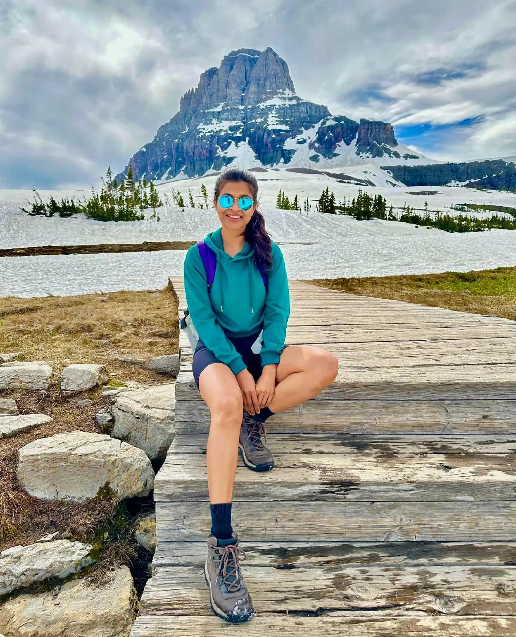 Artist Prachi Gawas seated on a wooden boardwalk in a snow-covered mountain in Glacier National Park